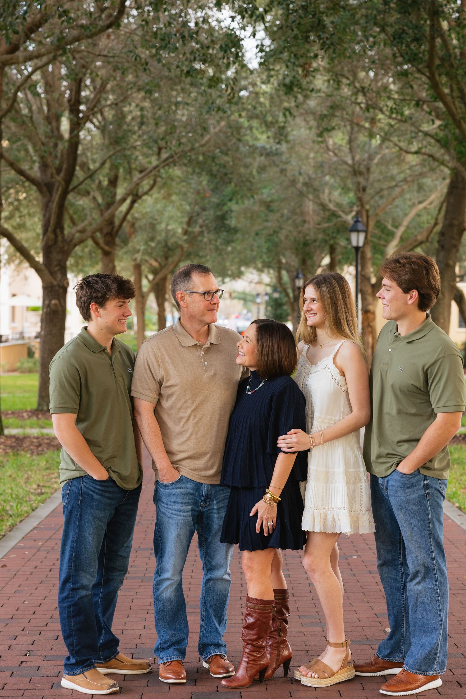 A group of people wearing casual clothing stand together on a brick pathway surrounded by trees.