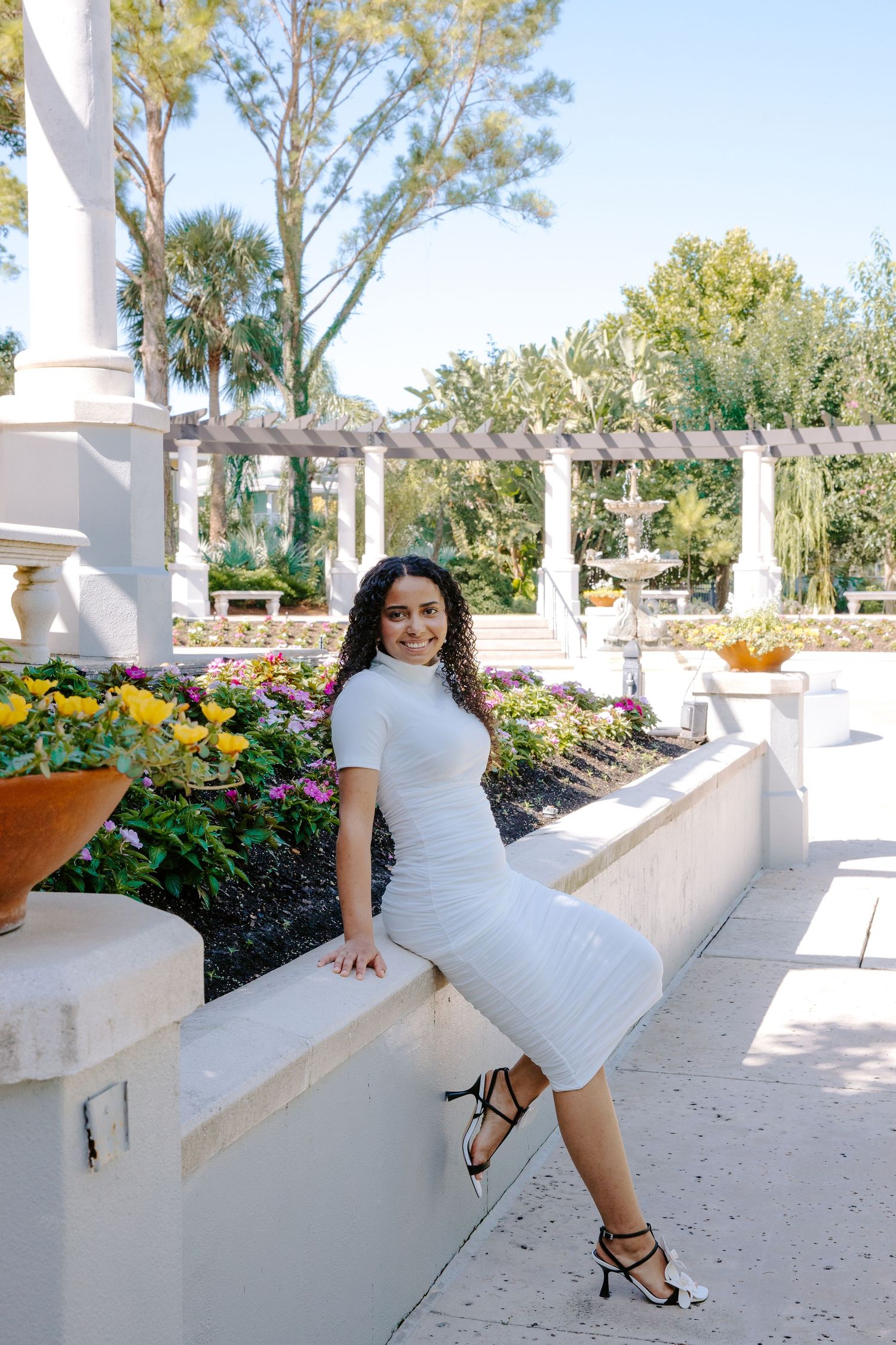 White dress photoshoot in an elegant garden terrace with columns and flowering planters.