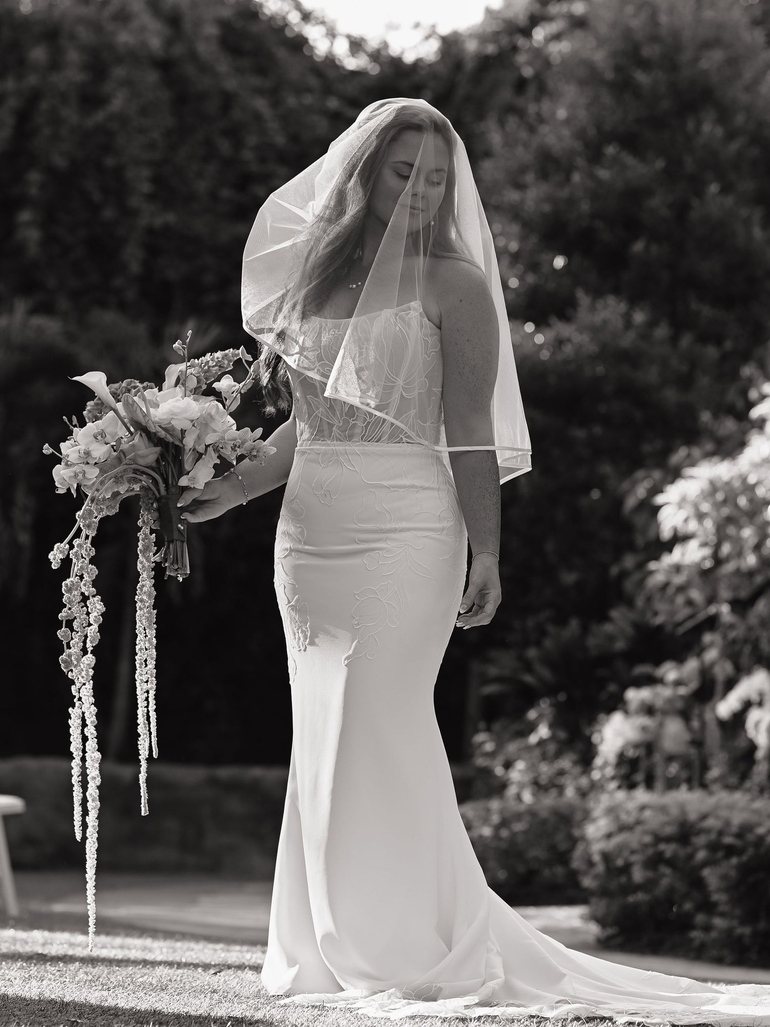 Black and white photo of an elegant wedding dress silhouette in a garden setting.