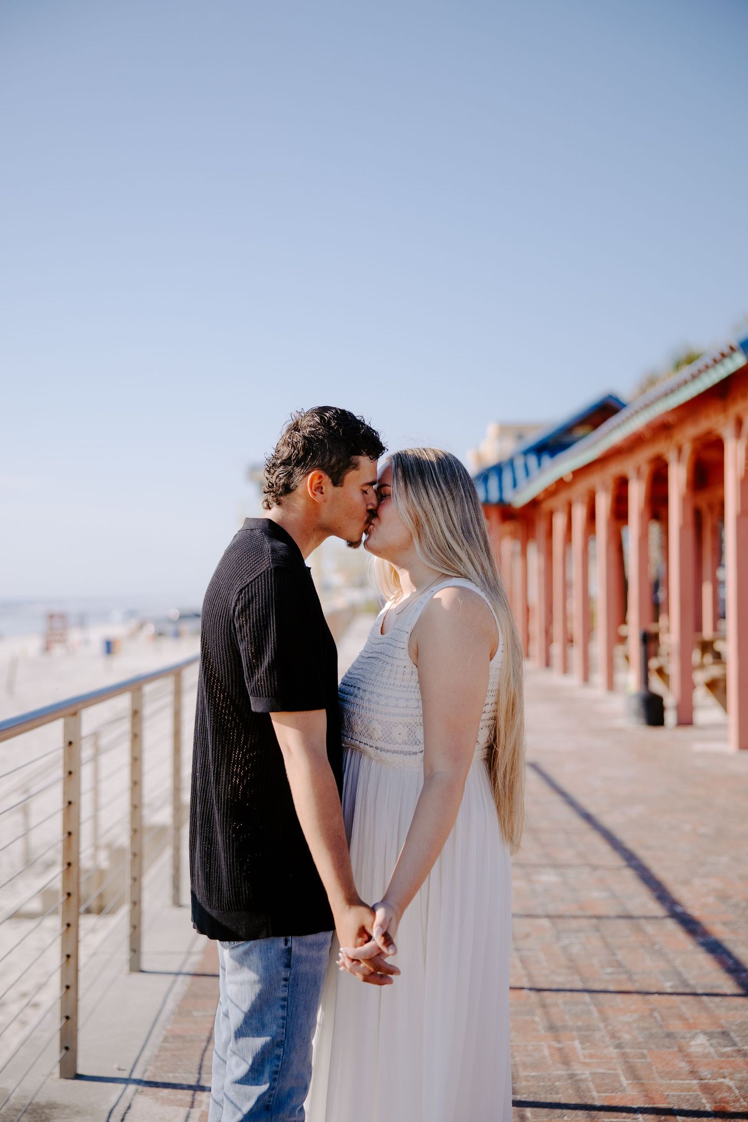Intimate couple portraits on a boardwalk with red buildings in background.