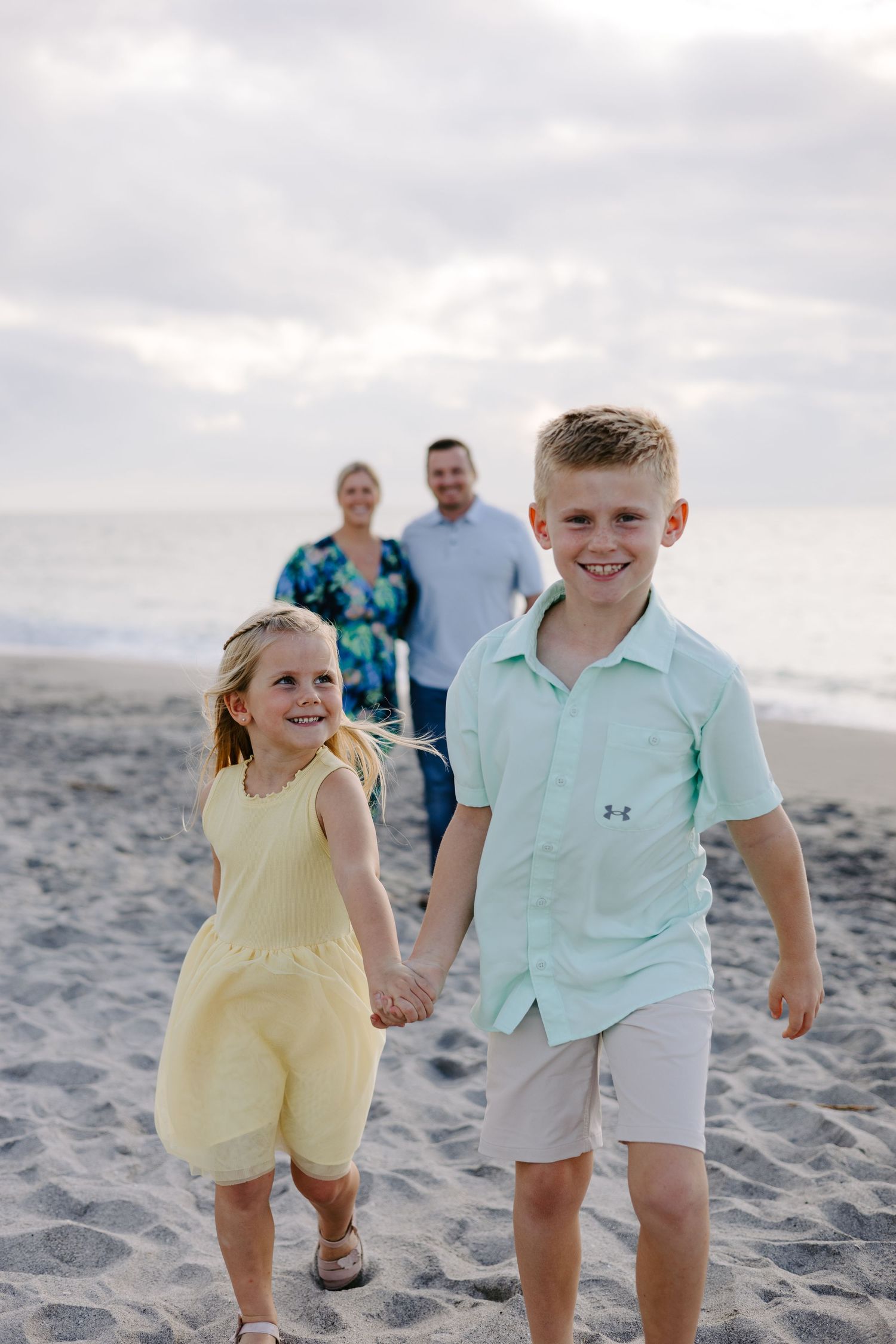 Children play and run together on a sandy beach during golden hour.