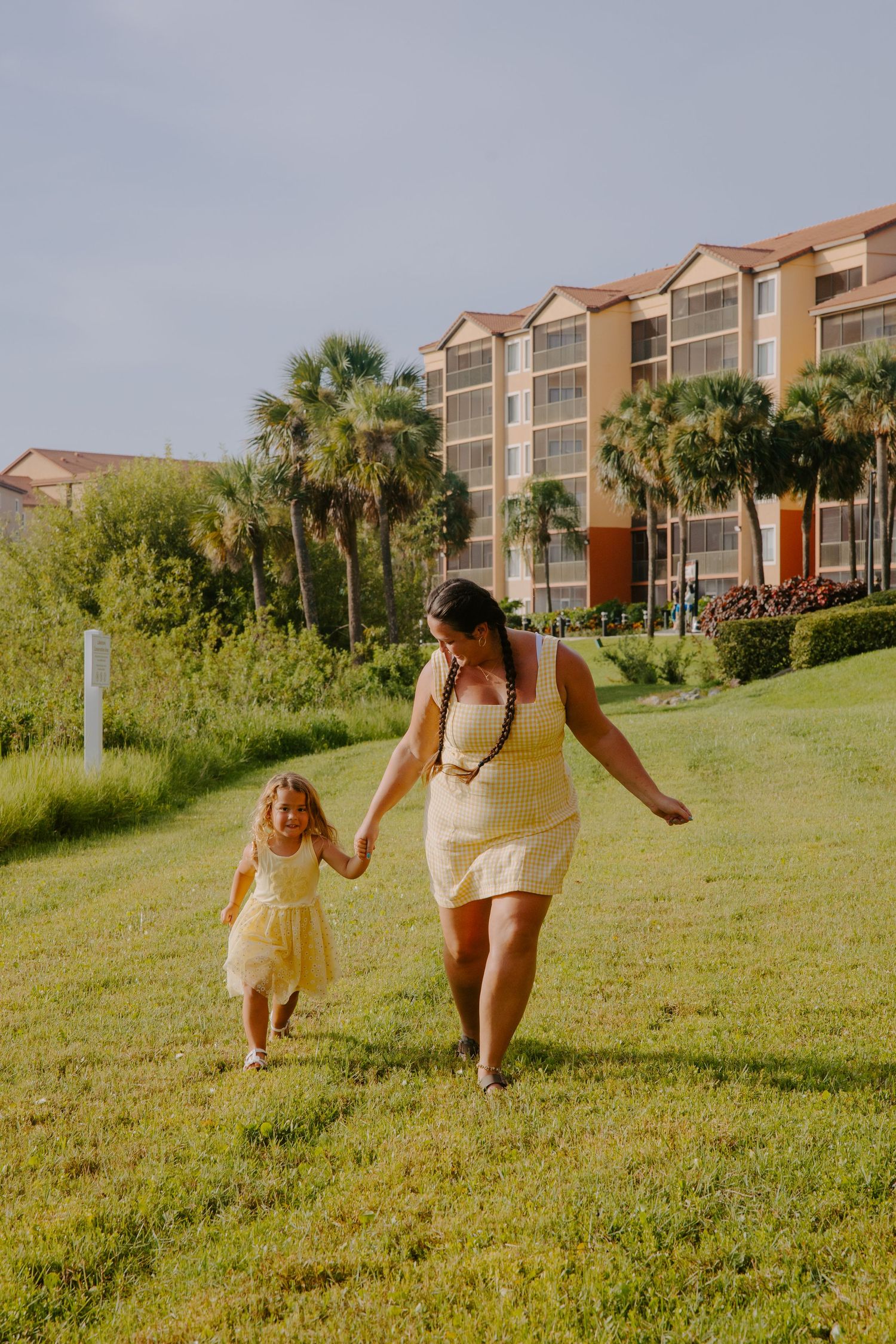 People walk and play on a grassy hill with beachside condominiums in the background.