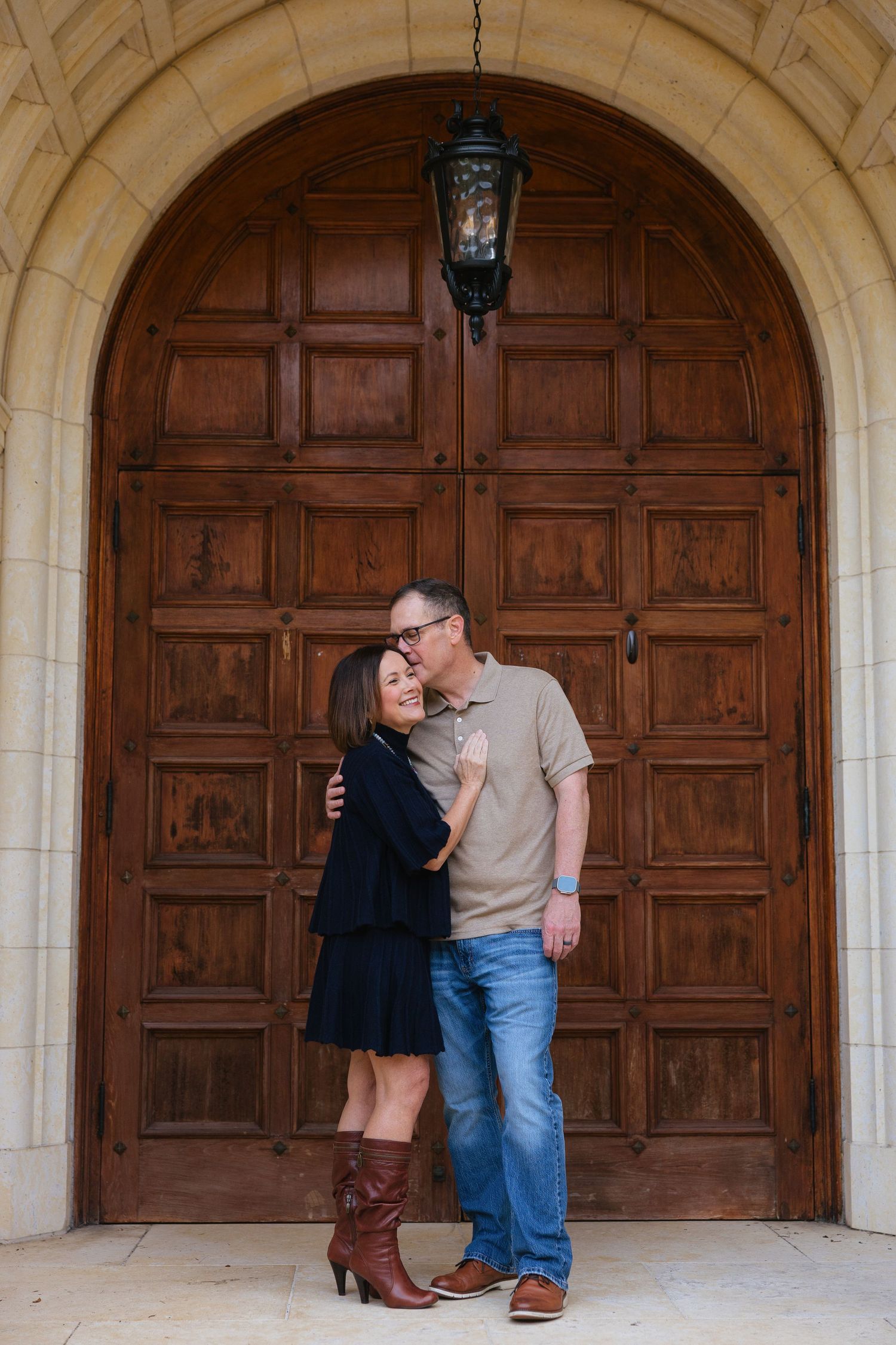 A couple shares a romantic moment in front of large wooden church doors with stone archways.