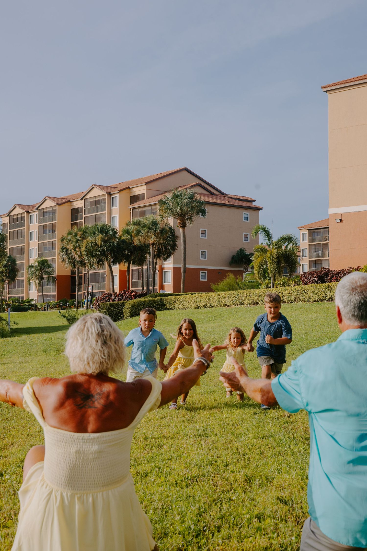 Group of people gather on a grassy lawn near coastal apartment buildings.