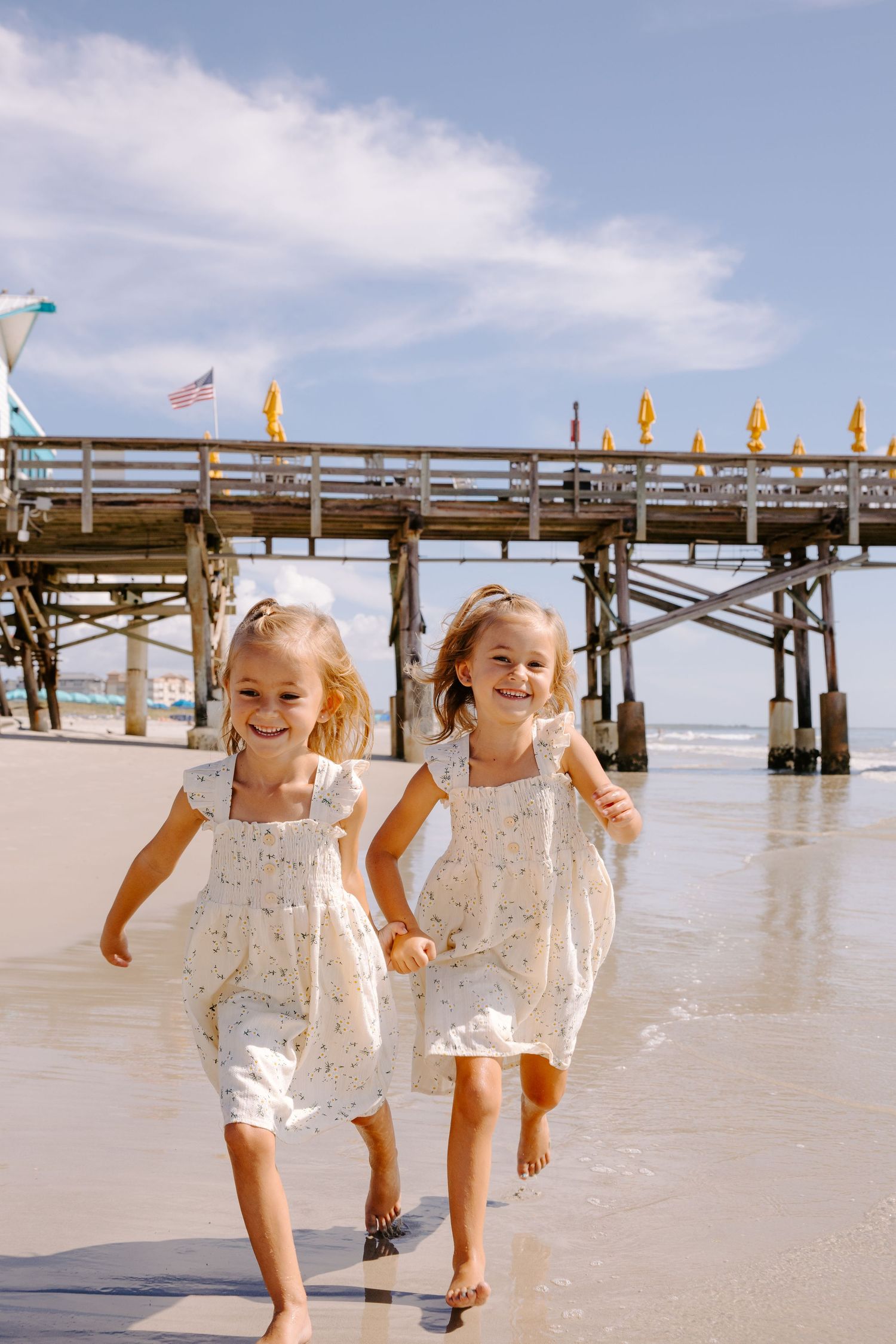 Two children play and splash in the ocean water near a pier with flags.