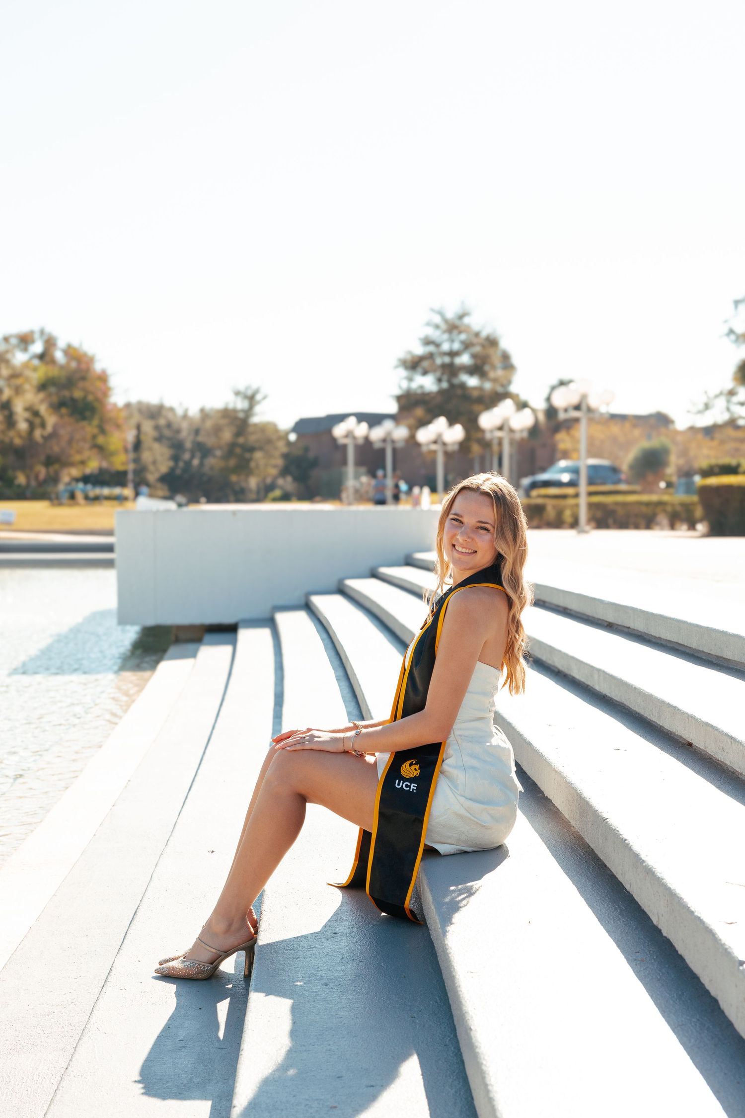 A woman in a black outfit poses on white concrete steps in bright sunlight.