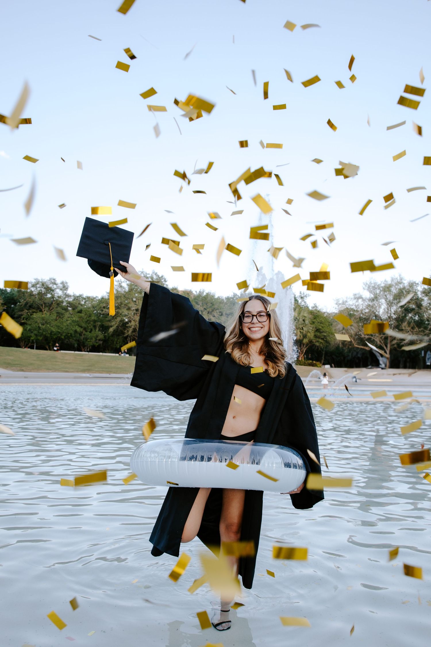 Gold confetti falls around graduate celebrating by lake.