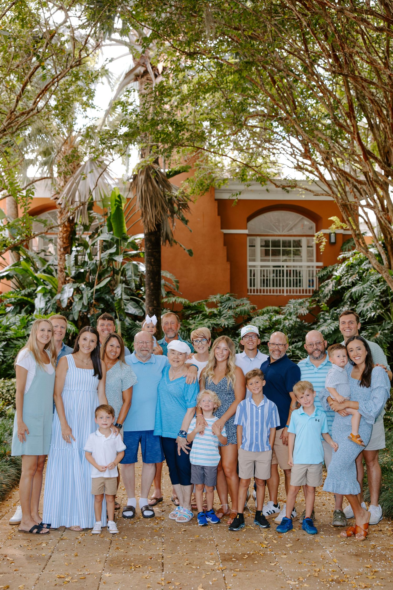 Large family group in coordinated blue and white outfits posed against lush tropical background.