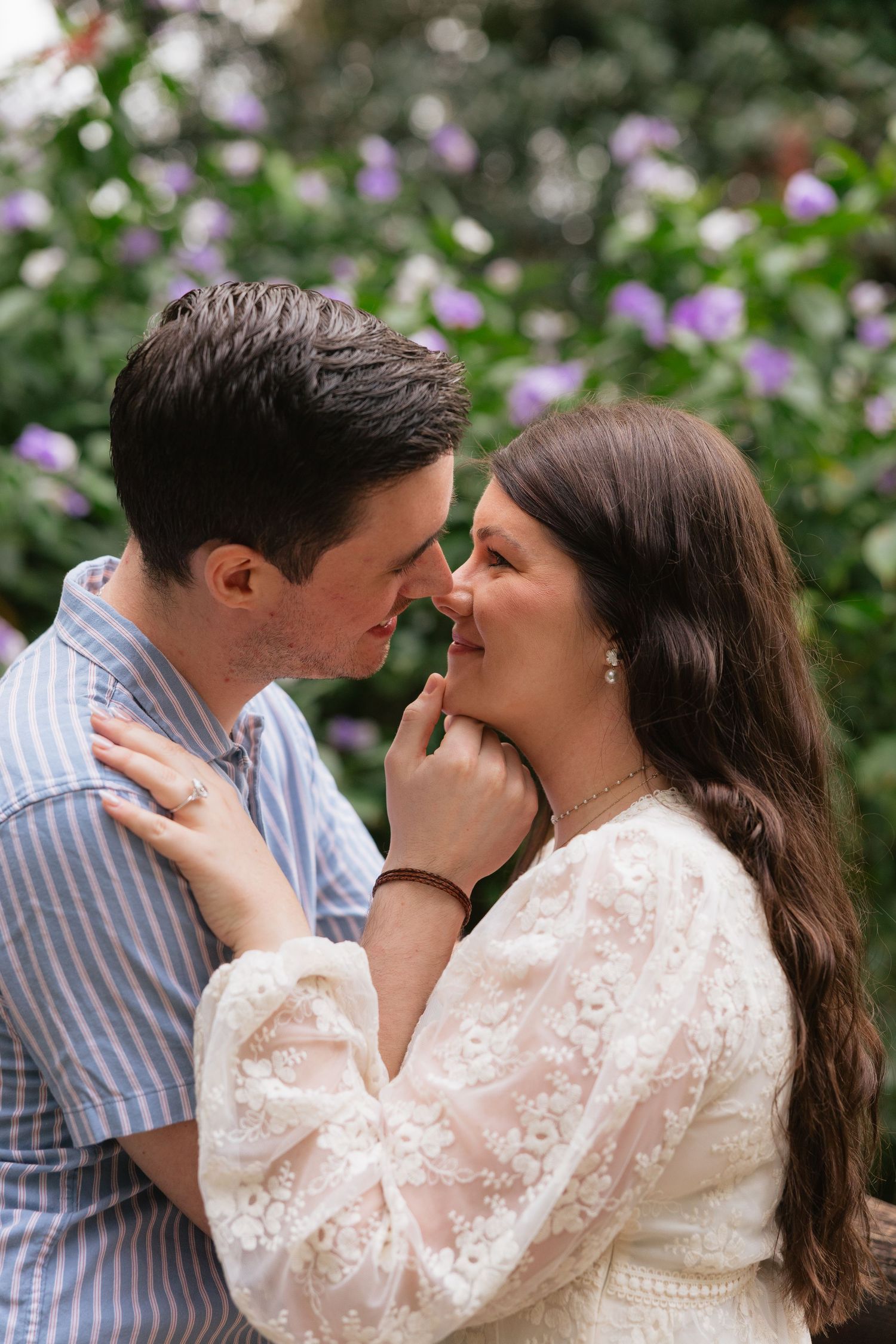 A romantic sequence of four photos showing a couple embracing and kissing in front of purple flowers and greenery.