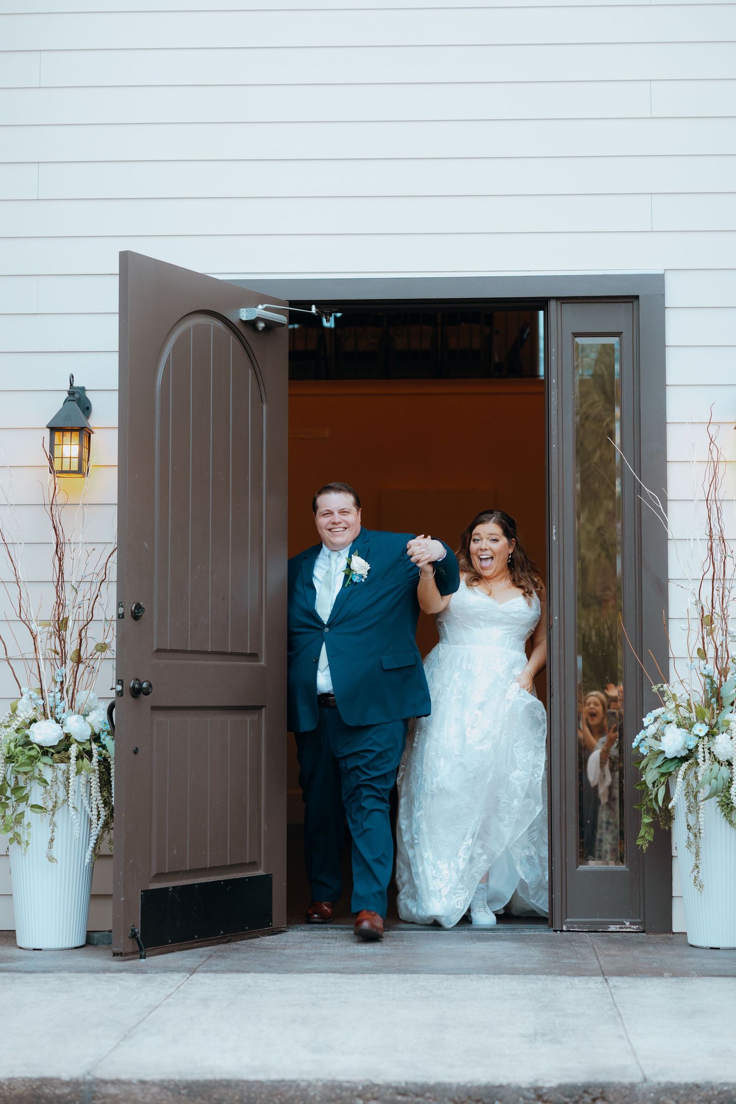Wedding couple makes grand exit through white barn doors decorated with floral arrangements.