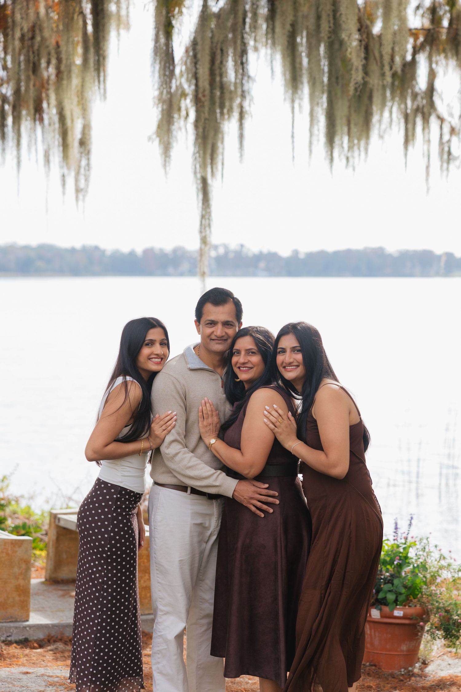 A group stands together by a lake with Spanish moss hanging from trees overhead and potted plants nearby.