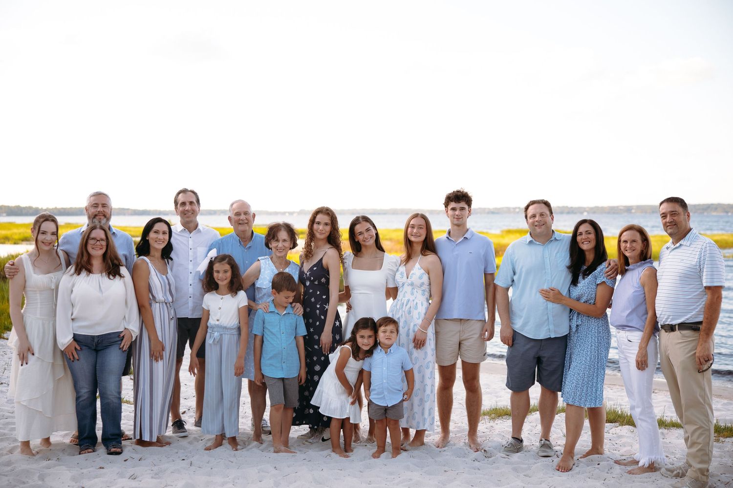 Extended family wearing coordinated blue and white outfits for beach portrait session.