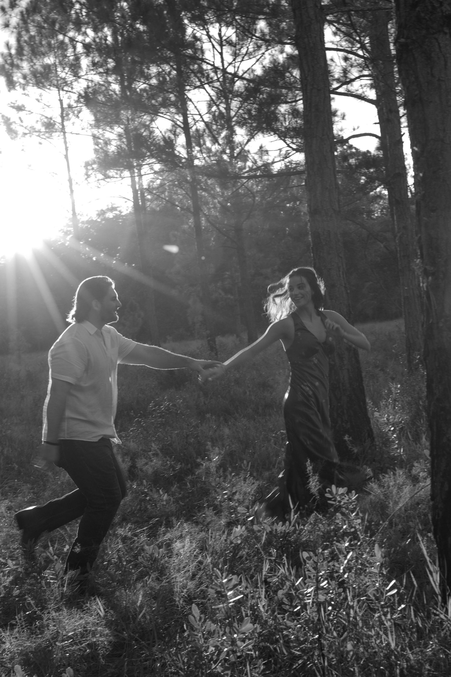 Two people dance together in a sunlit forest clearing with rays of light streaming through tall pine trees.