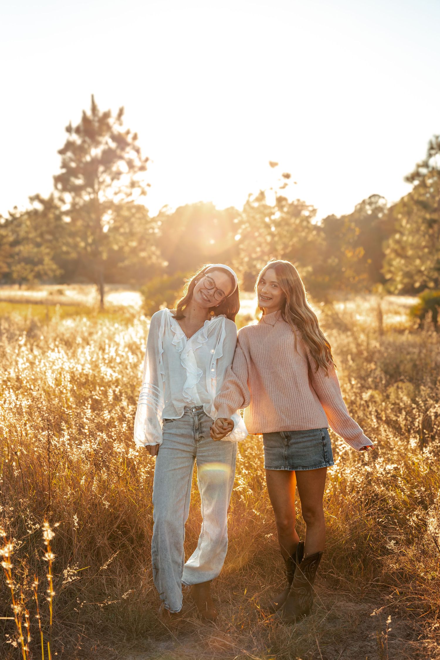 Two friends walking together through a golden sunlit field at sunset wearing casual summer outfits.