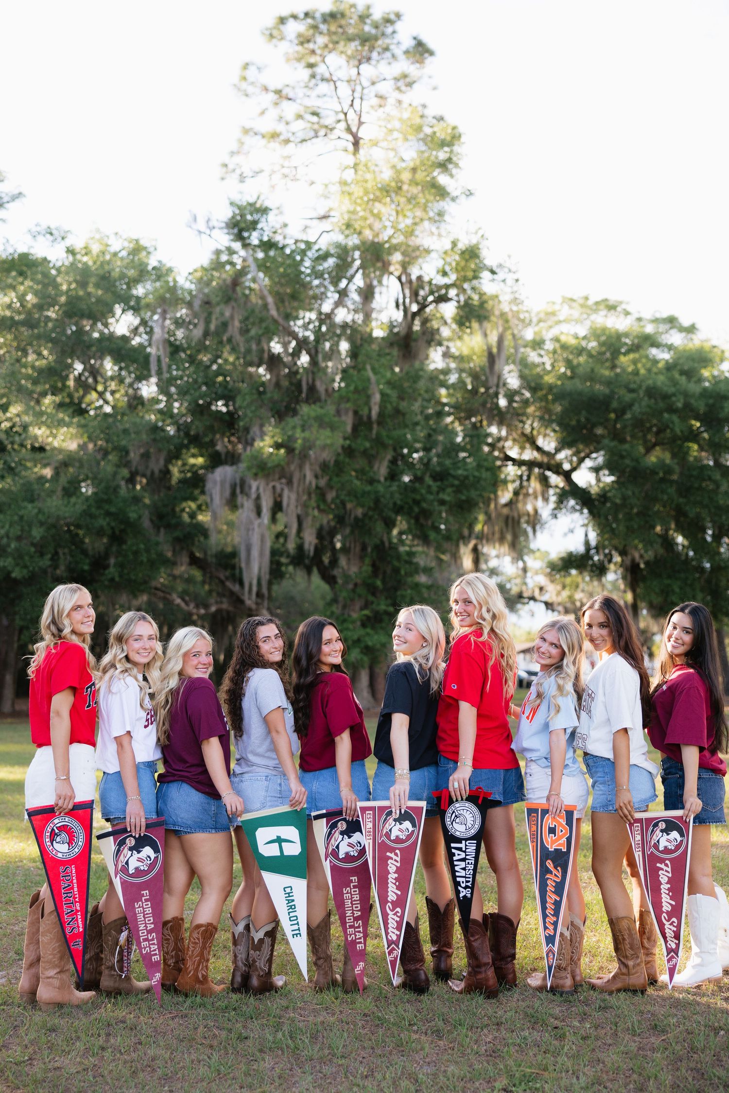Group of young women posing outdoors holding colorful college pennants including Florida State and Charlotte.