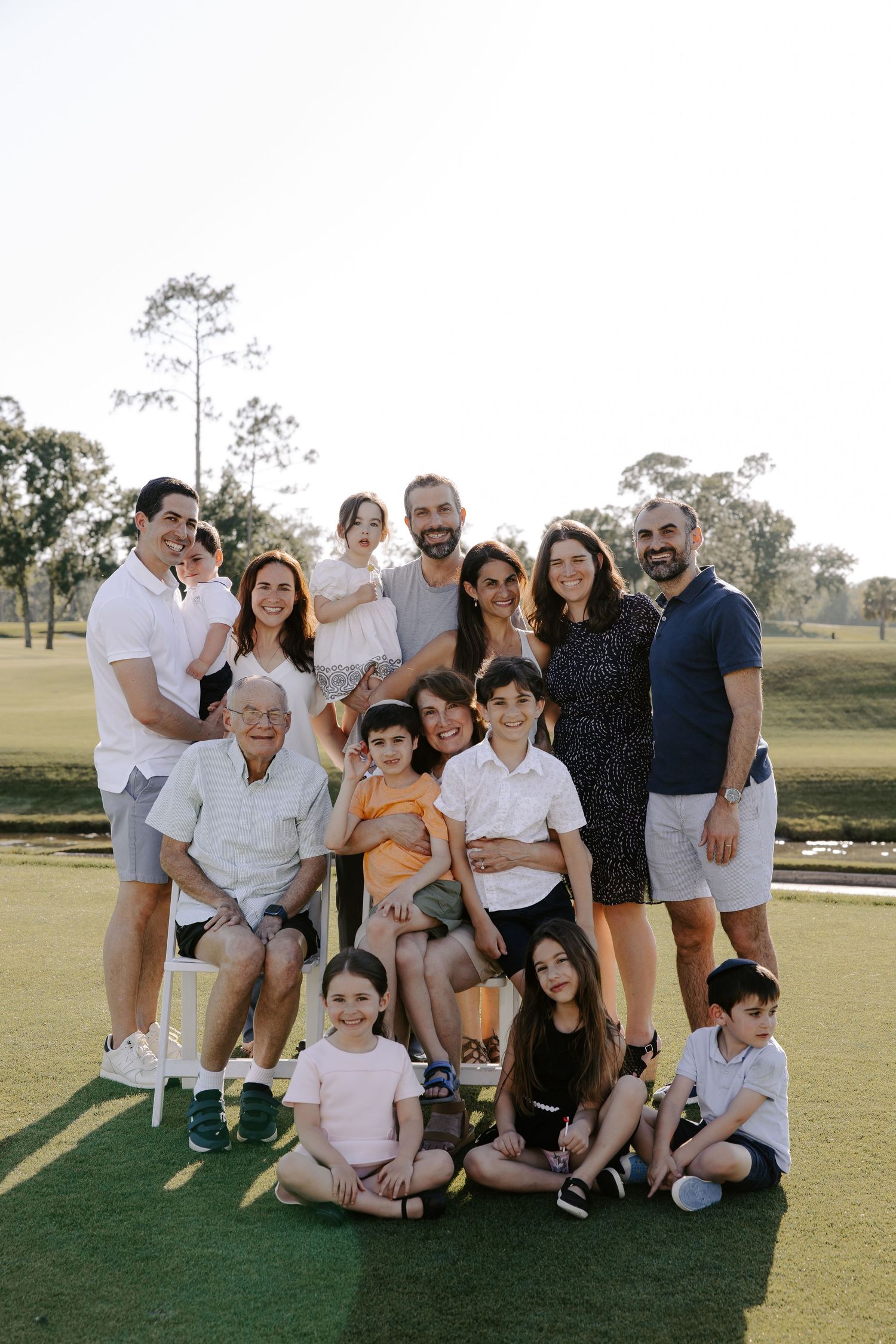 Large family group posing together on green grass during an outdoor photo session.