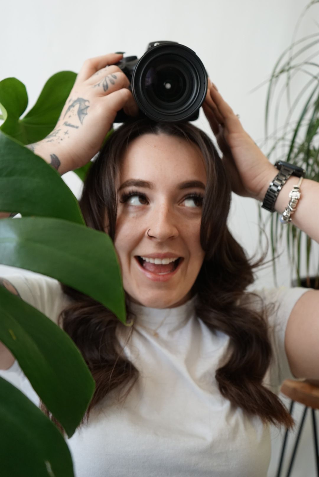 Close-up of photographer holding a professional camera behind green foliage, representing Fern & Frame Photography