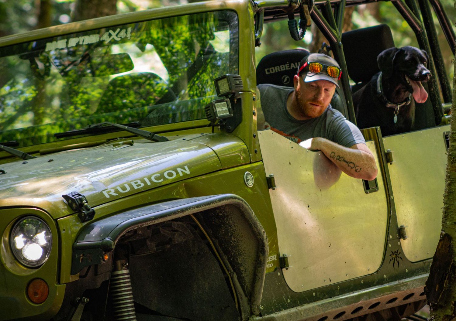 Young man driving jeep off road and his dog hanging out the back window