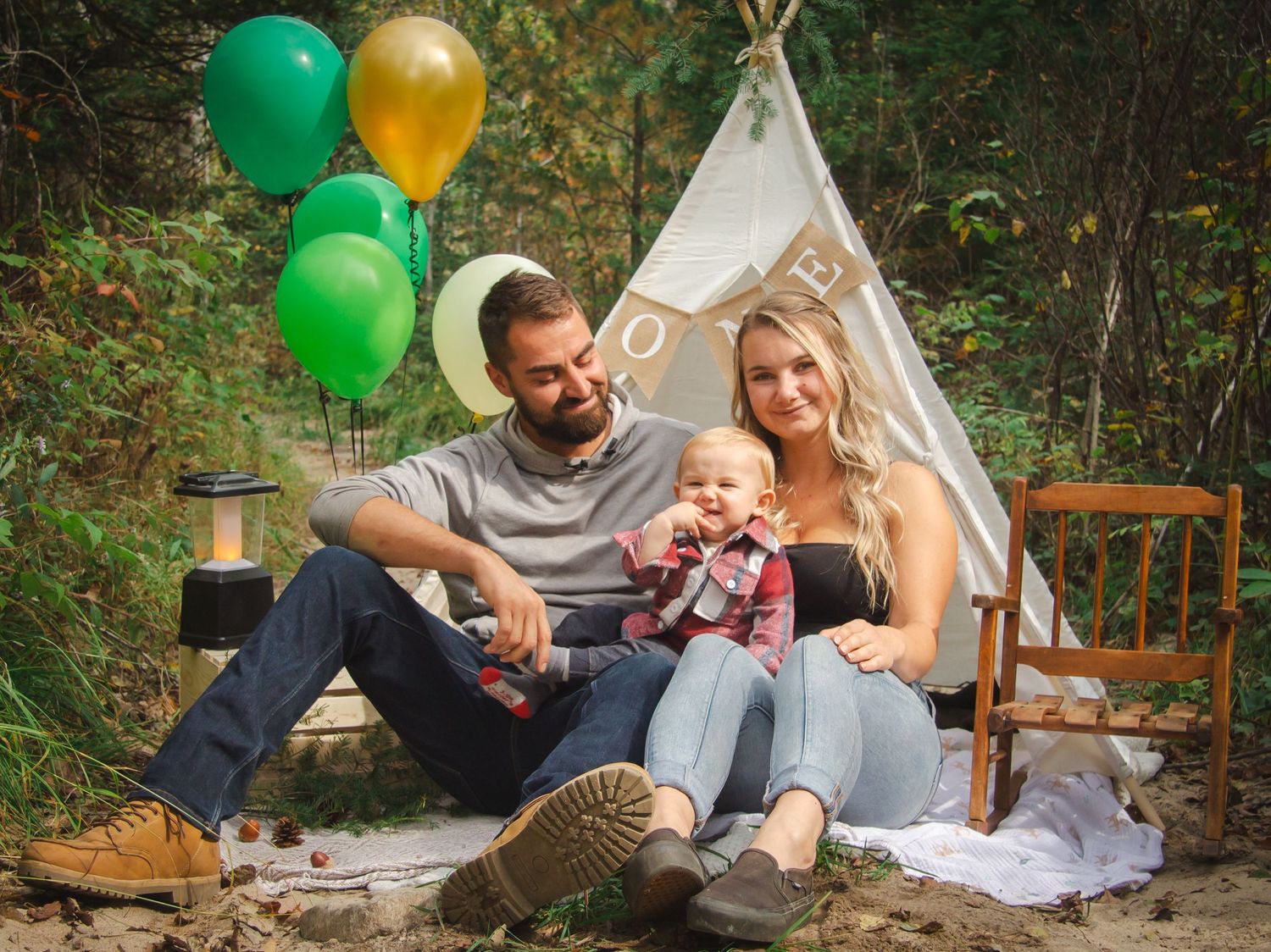 mother, father and baby sitting infront of decorated tent in the forest