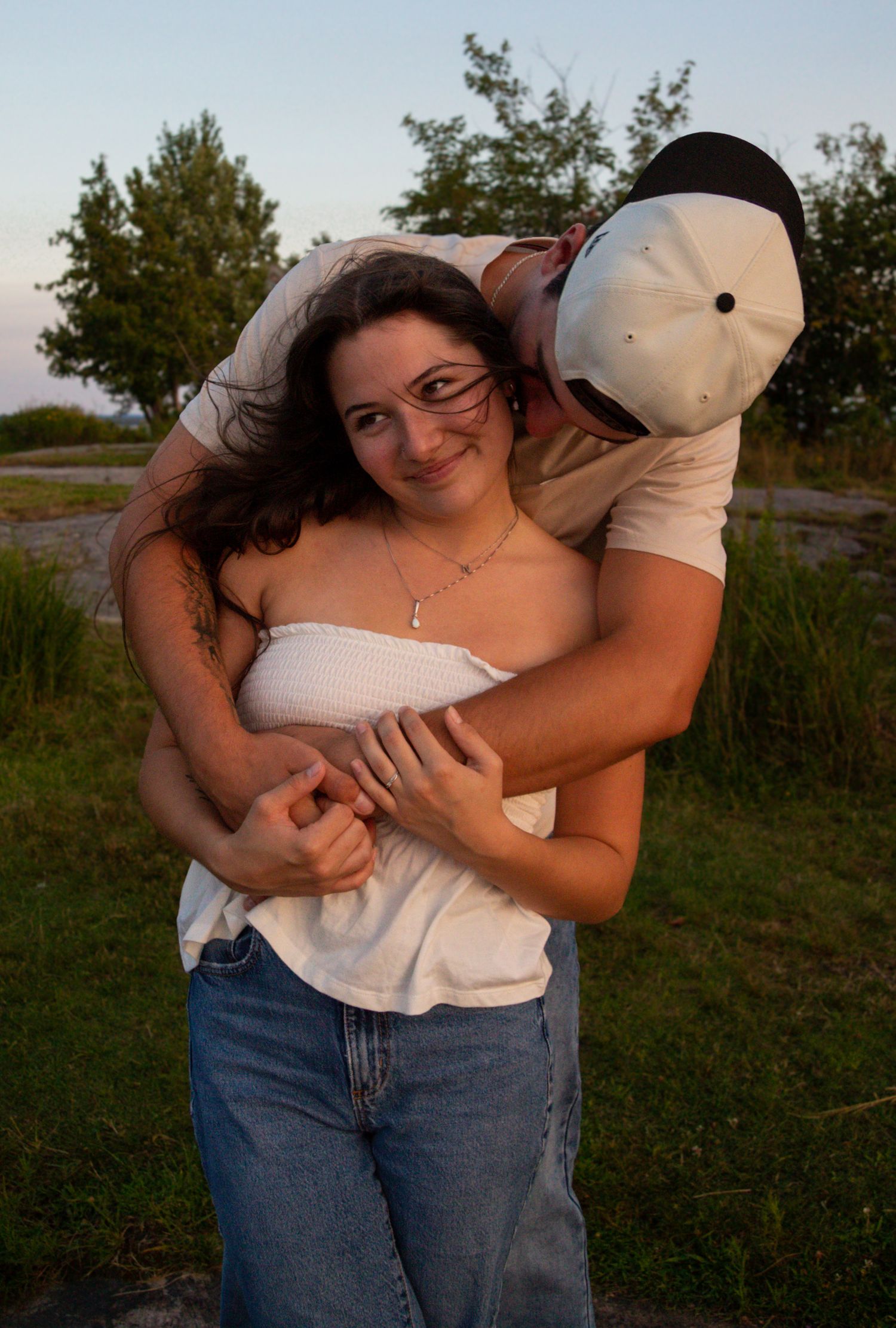 couple at the beach at sunset, man is hugging girl front behind