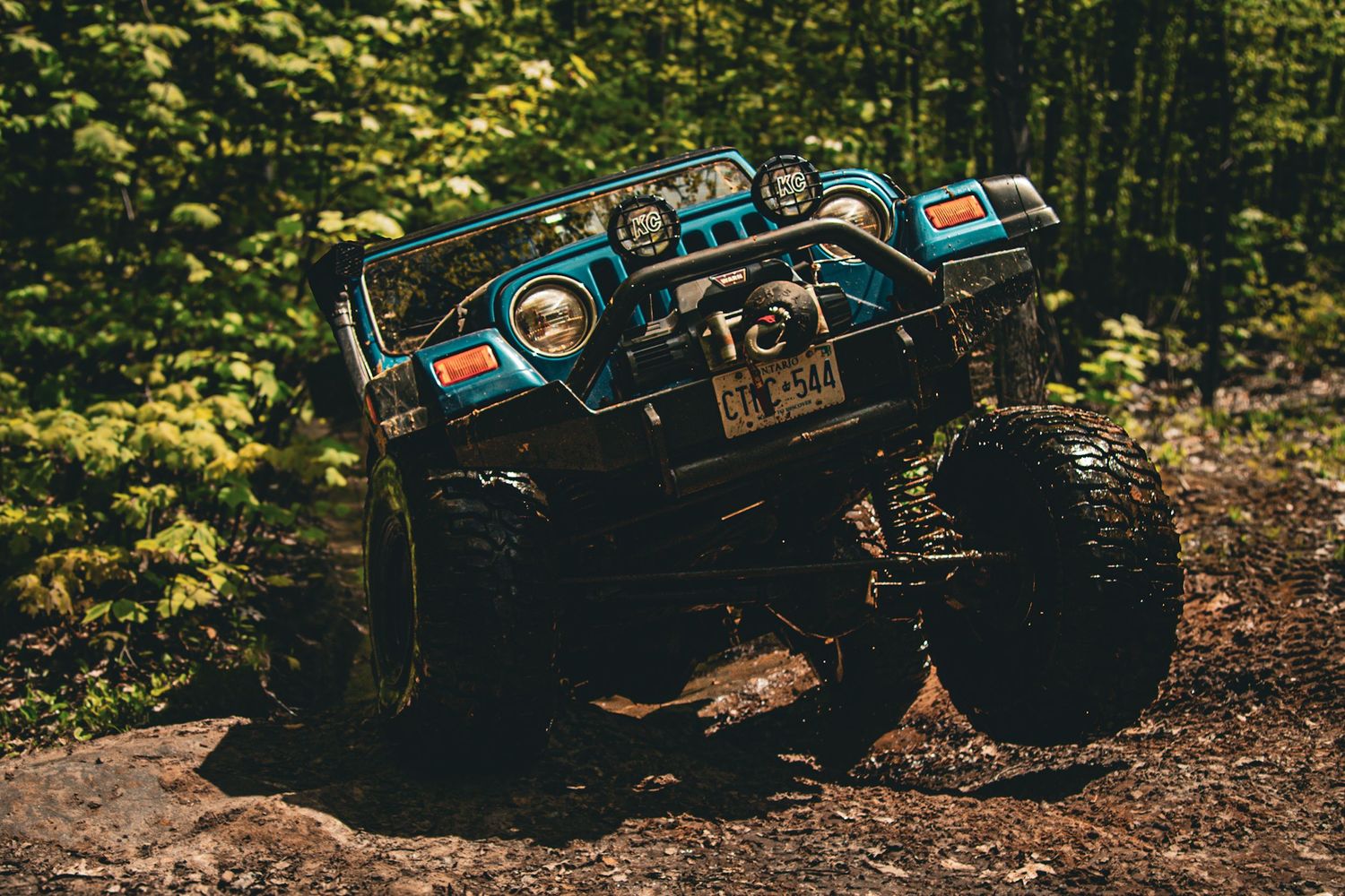 blue jeep jumping over rocks in forest
