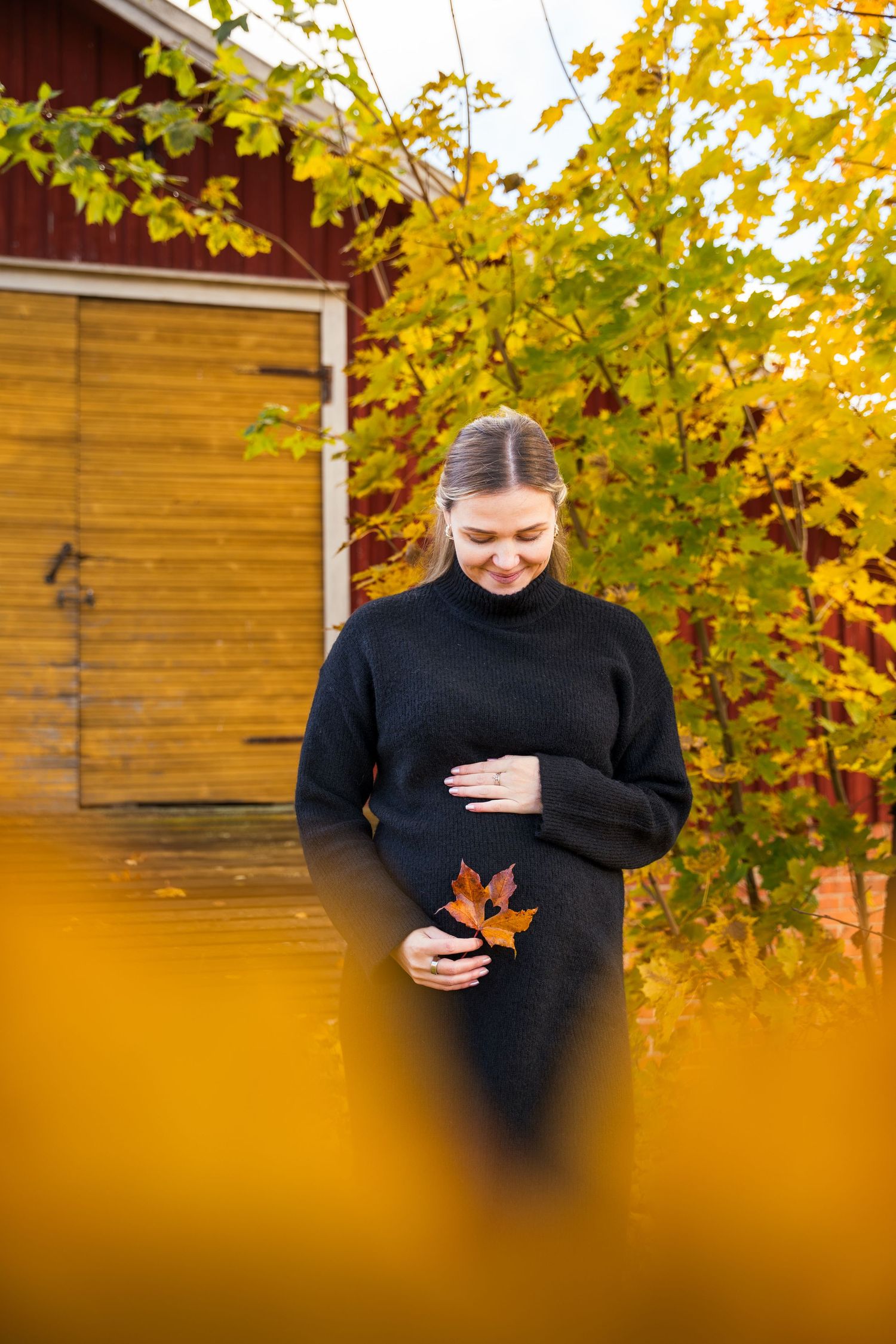 Odottava äiti syleilee vatsaansa syysmaisemassa