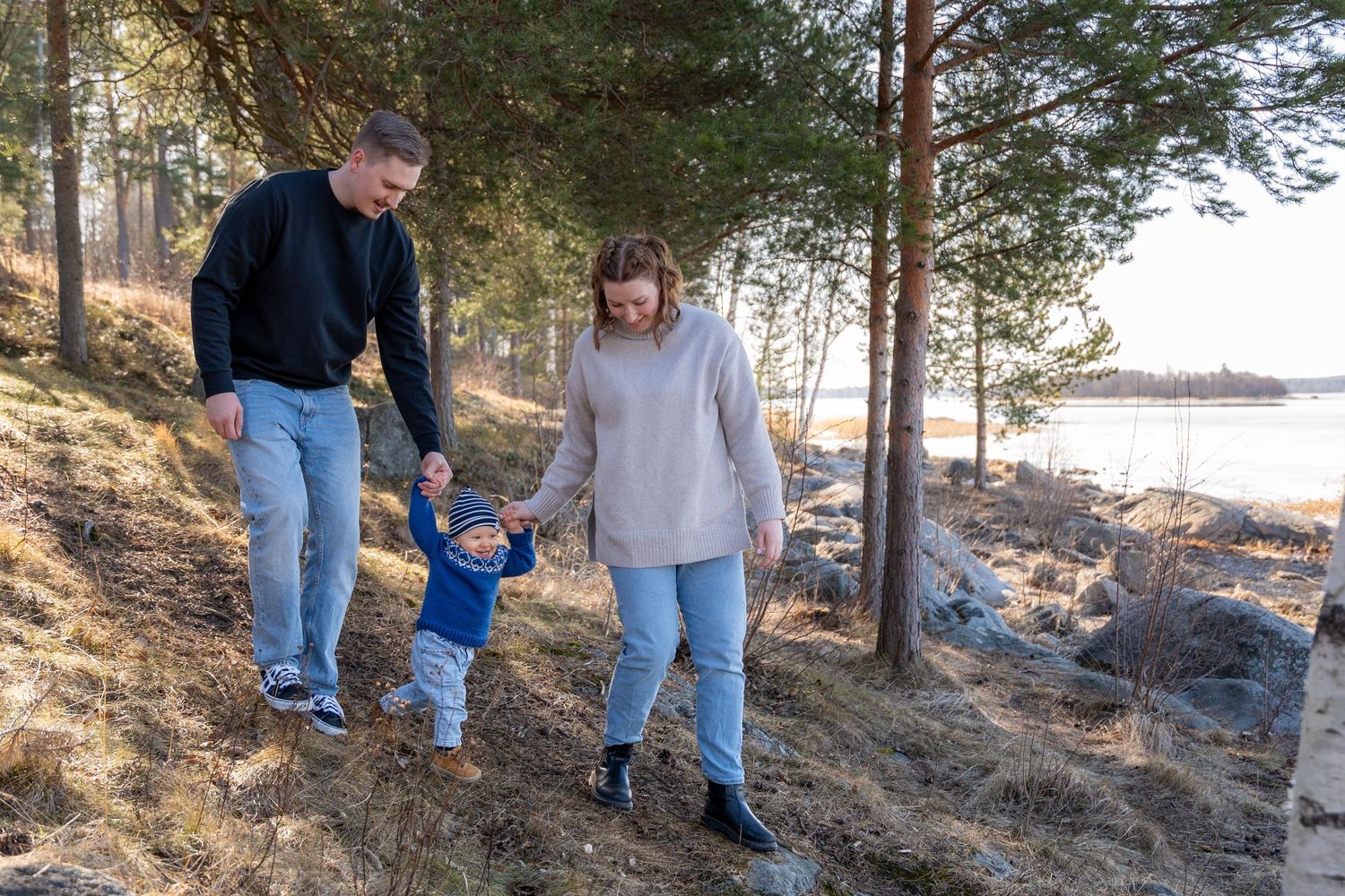 Perhe kävelee mäkeä alas. Poika keskellä kädet vanhempien käsissä.