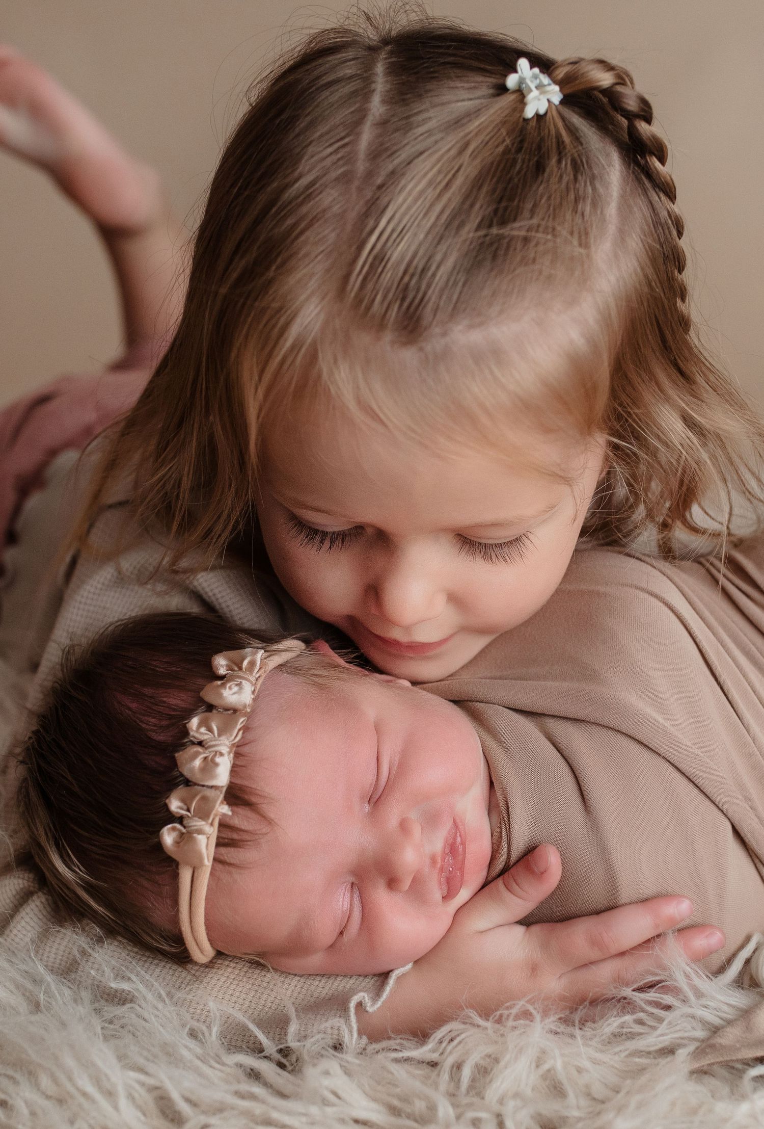 Two children sharing a tender moment on soft fur bedding with matching pearl floral headbands.