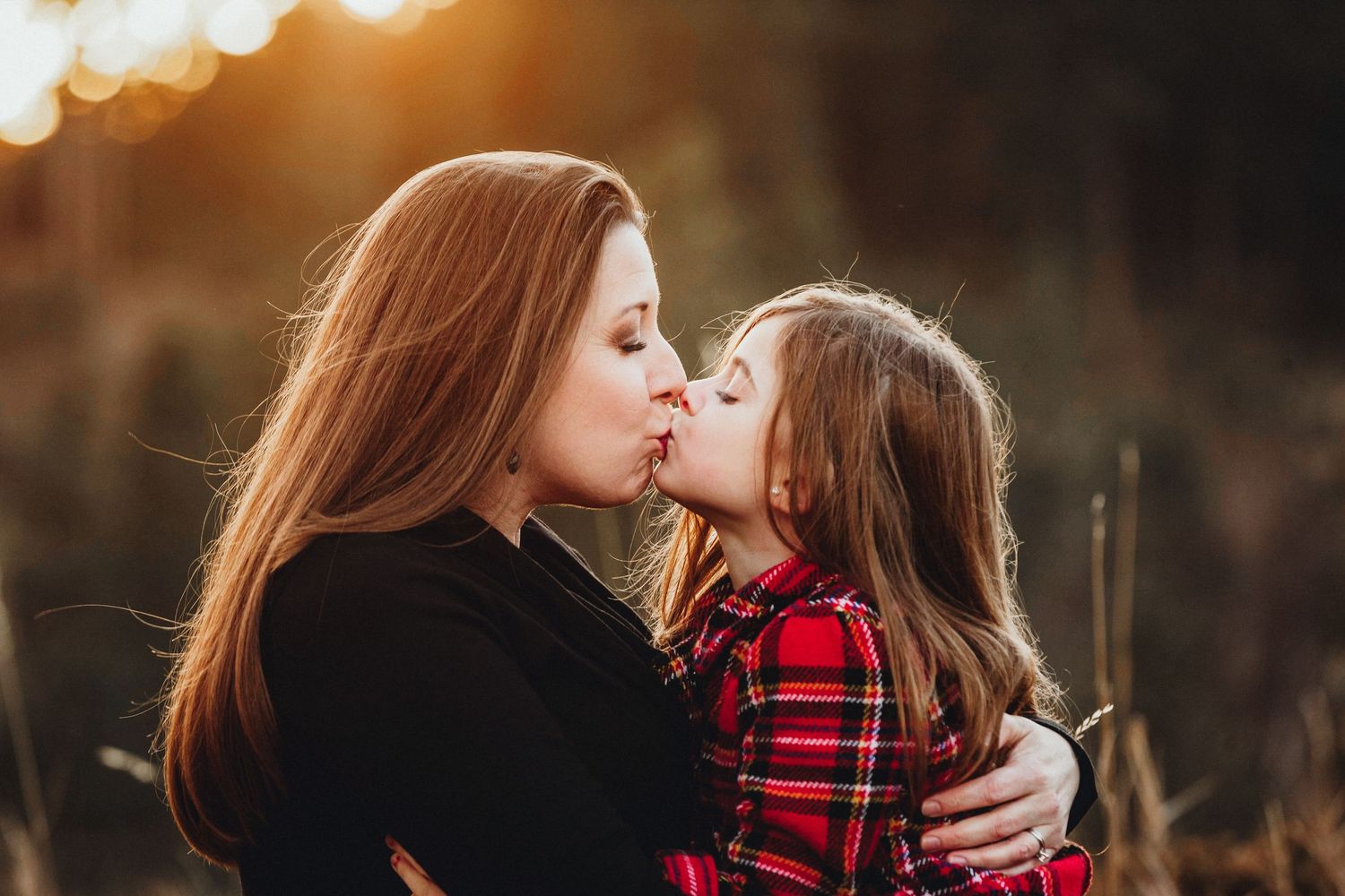 A tender moment between parent and child wearing coordinating red and black outfits against a warm golden sunset.