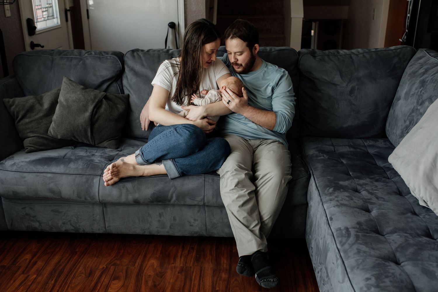 Couple lounges together on gray sectional sofa while looking at phone in cozy living room.