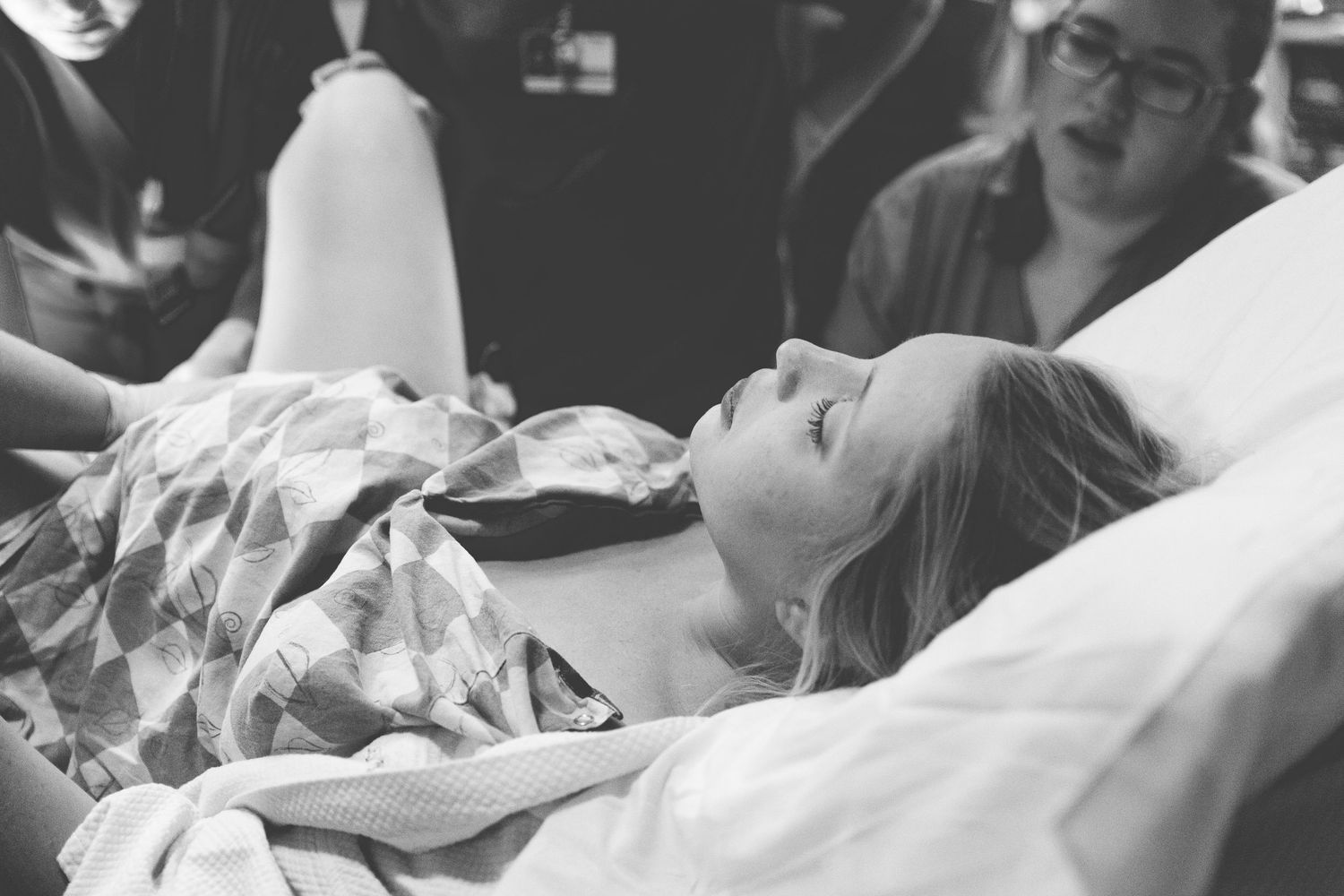 Black and white photo showing someone lying in a medical bed wearing a hospital gown during a medical procedure.