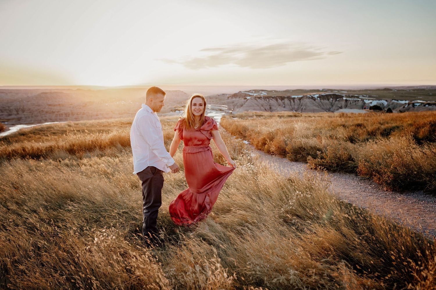 A couple shares a romantic moment in golden fields during sunset as warm light illuminates the landscape.