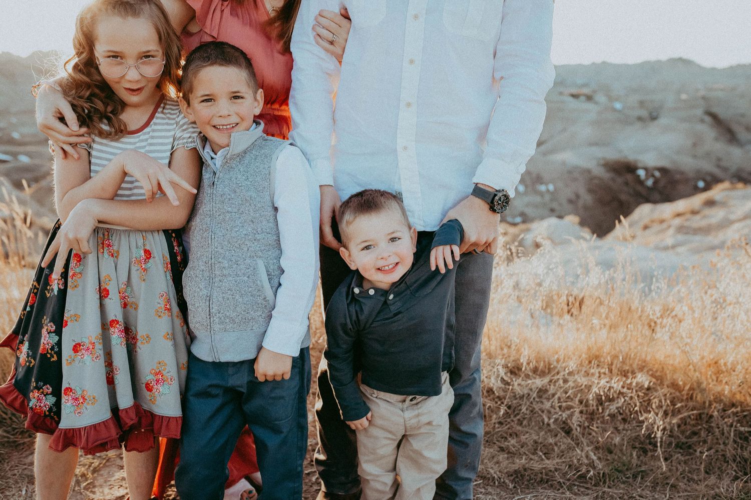 Children and adults pose together outdoors in a field with dry grass and blue sky at sunset.