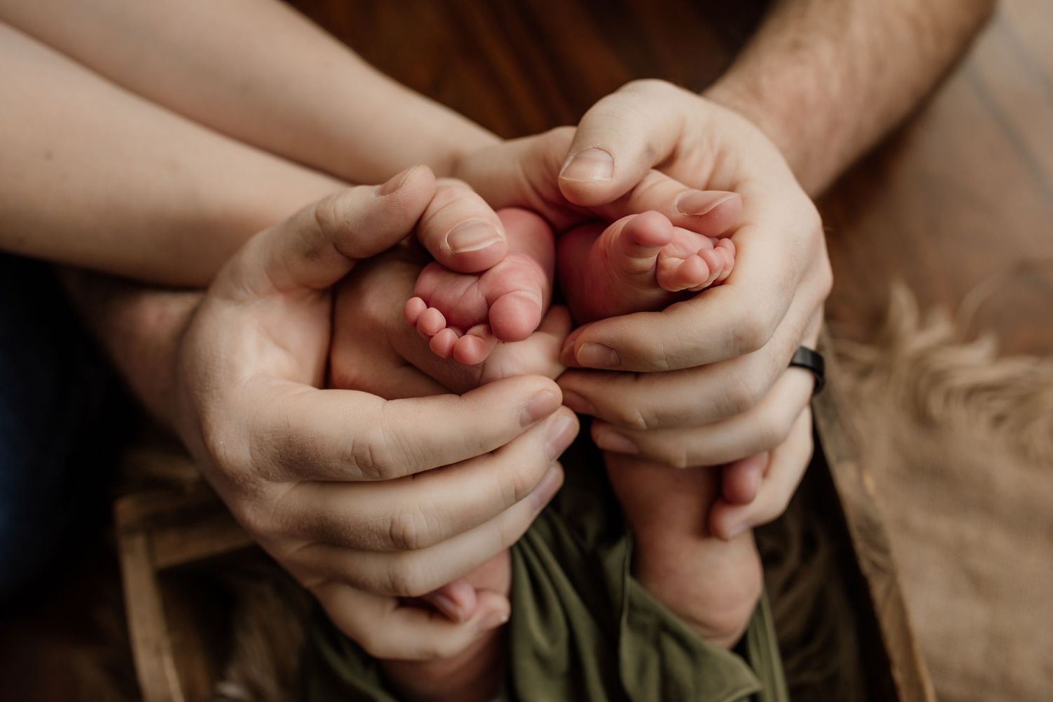 Adult hands gently holding tiny newborn baby feet with soft natural lighting.