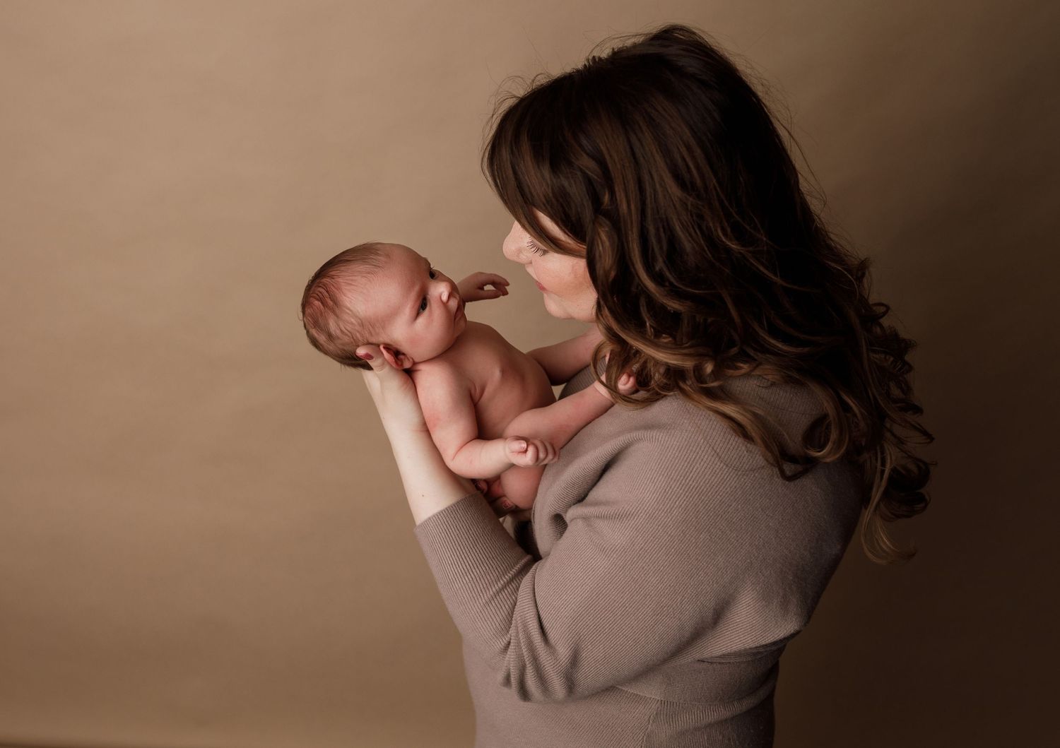 A tender moment captured in warm lighting shows a gentle interaction with a sleeping newborn baby.