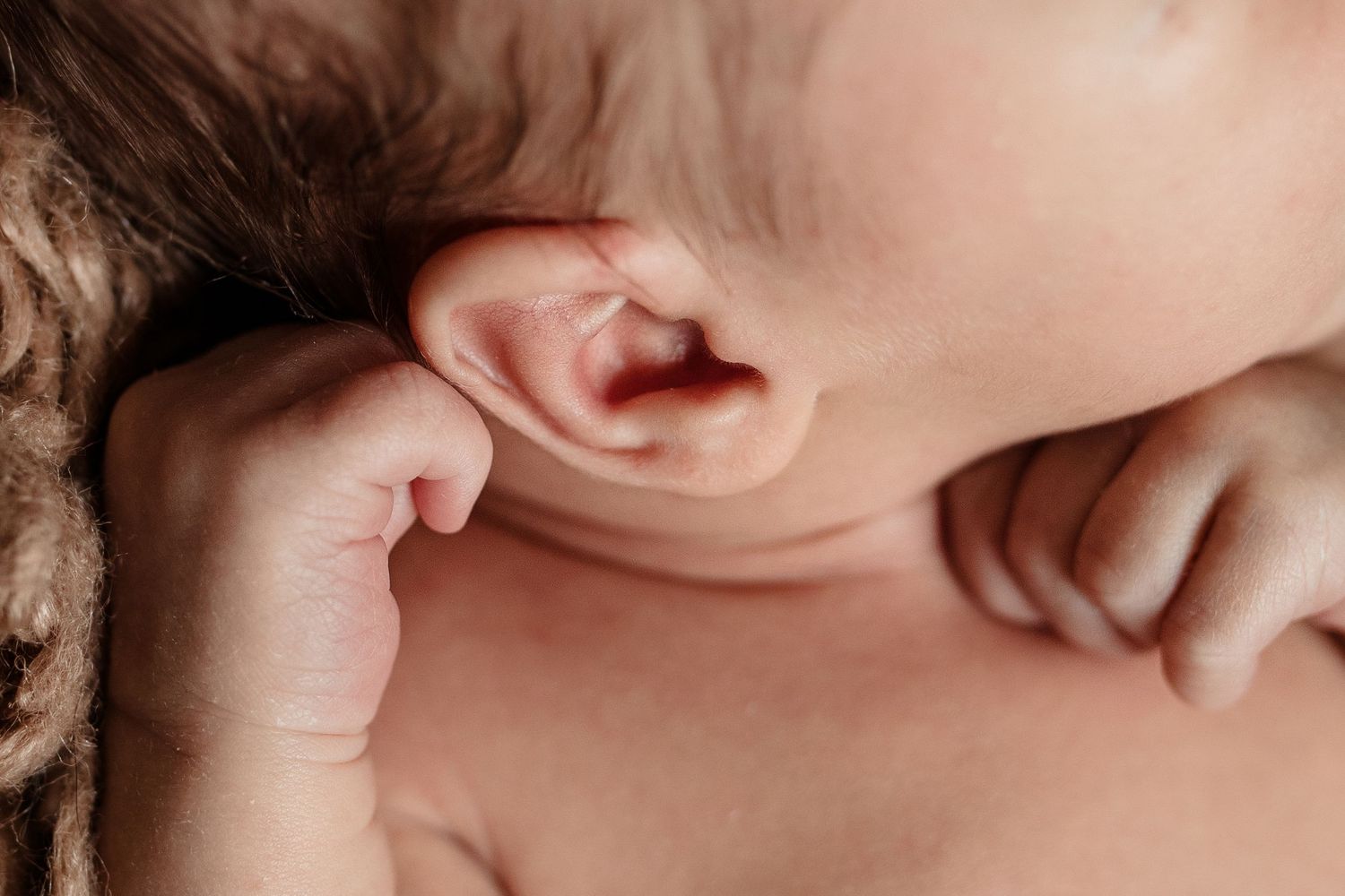 Close-up macro photograph of a baby's ear and tiny hand against soft skin.