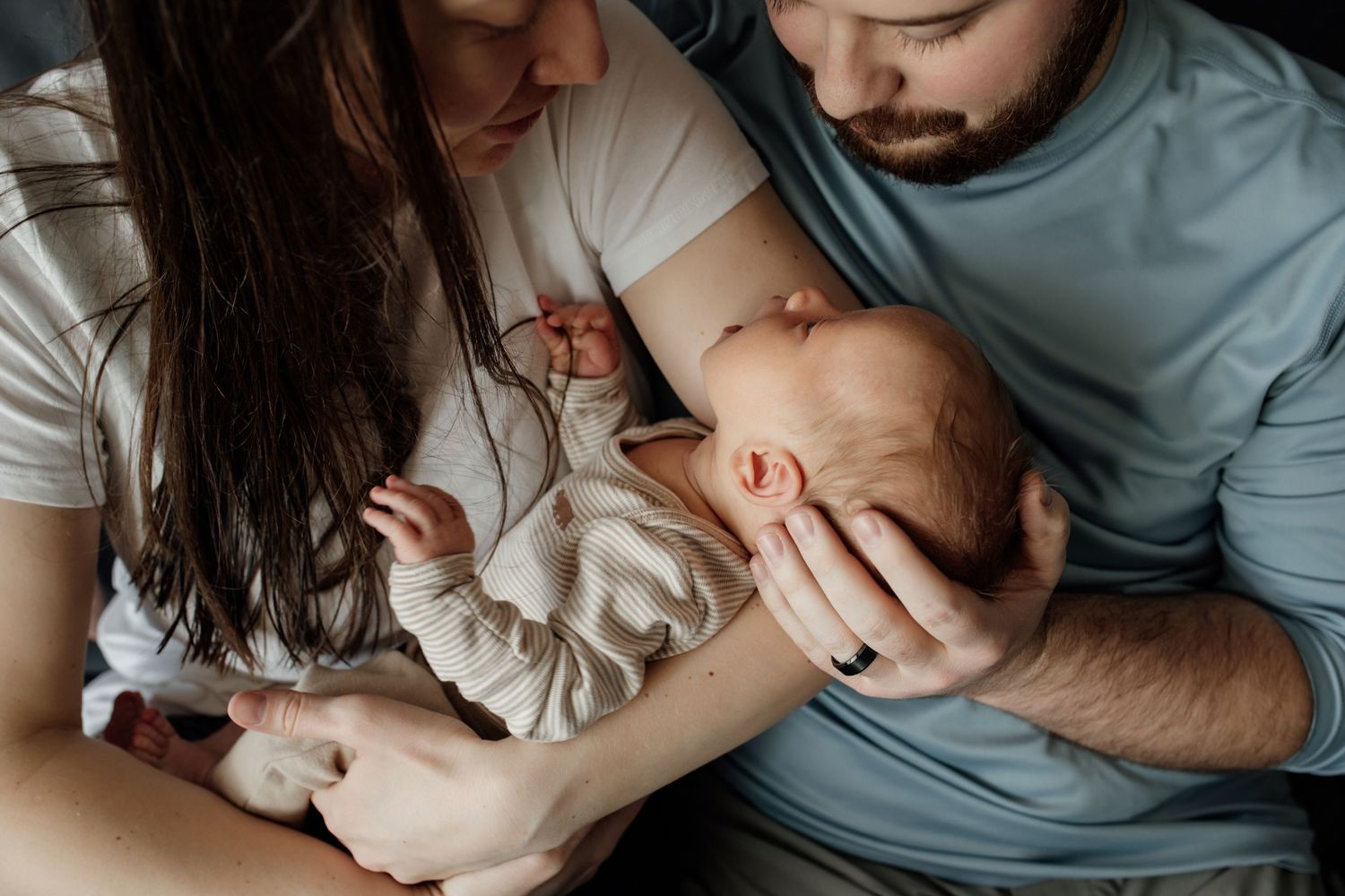 Parents tenderly holding and gazing at their newborn baby in an intimate indoor setting.