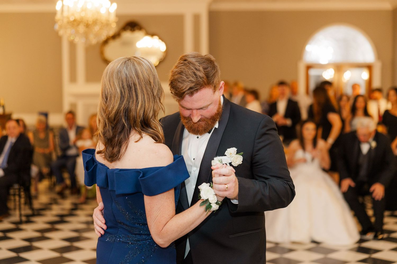 Wedding guests share emotional embraces during a reception in a beautifully lit ballroom.