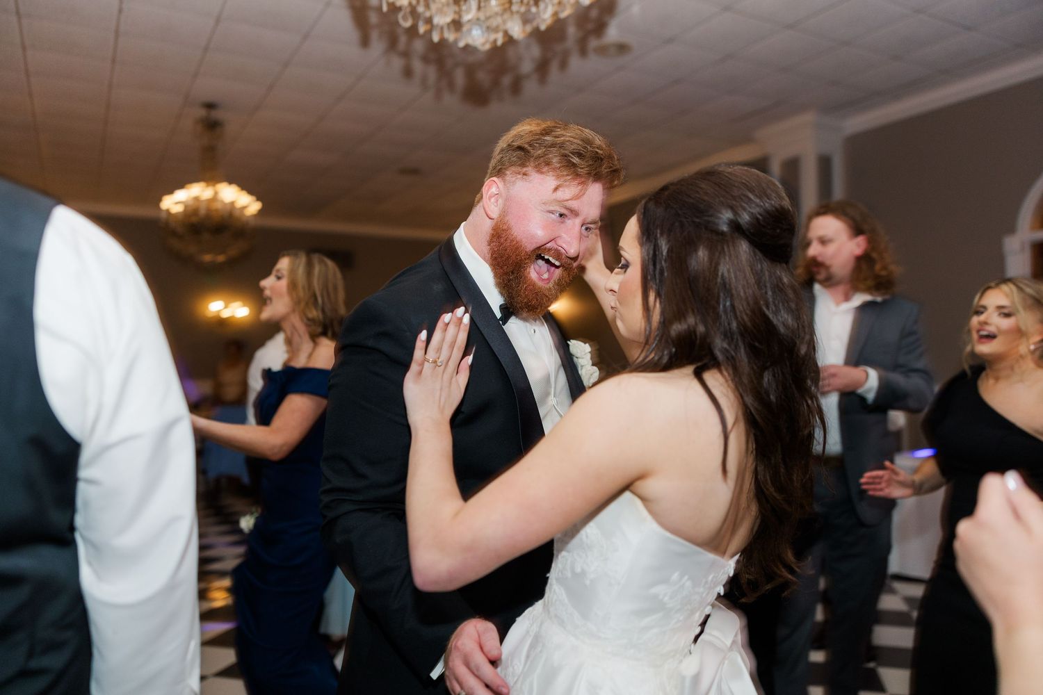 Wedding guests dancing and celebrating at an indoor reception with chandeliers.