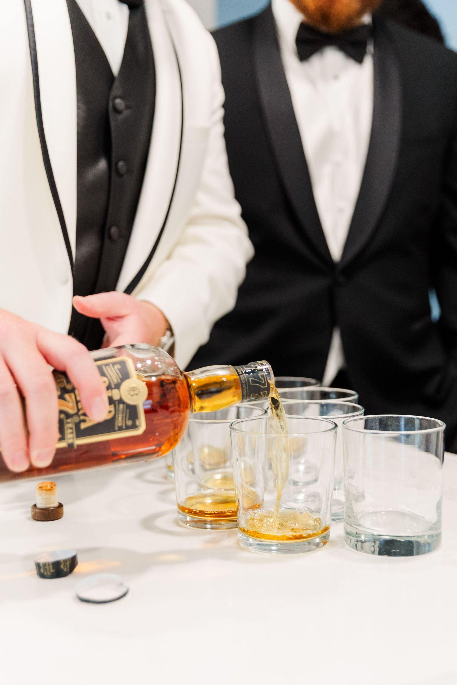 Close-up of formal tuxedos pouring whiskey into glasses at an elegant event.