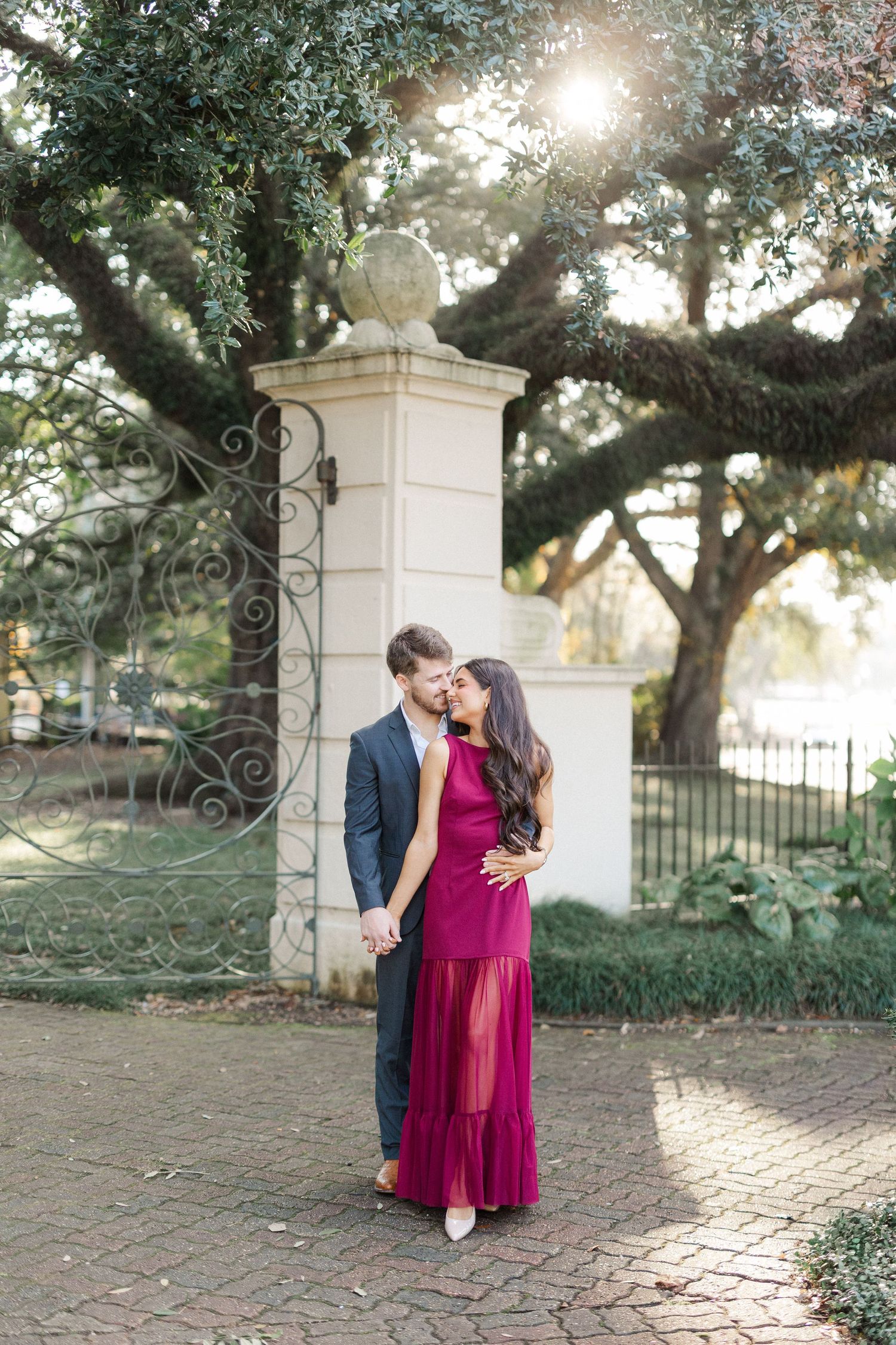 Romantic couple embraces near white stone pillars in a garden setting during golden hour.