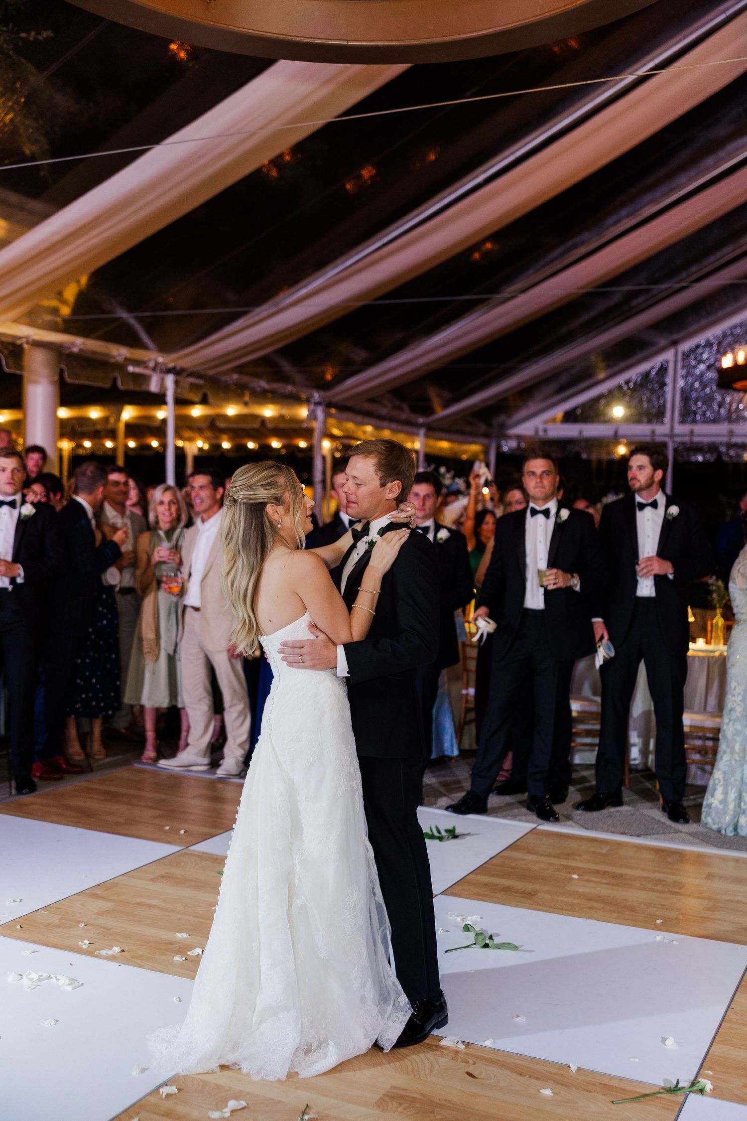 Wedding reception first dance under a draped tent with guests watching from the sides.