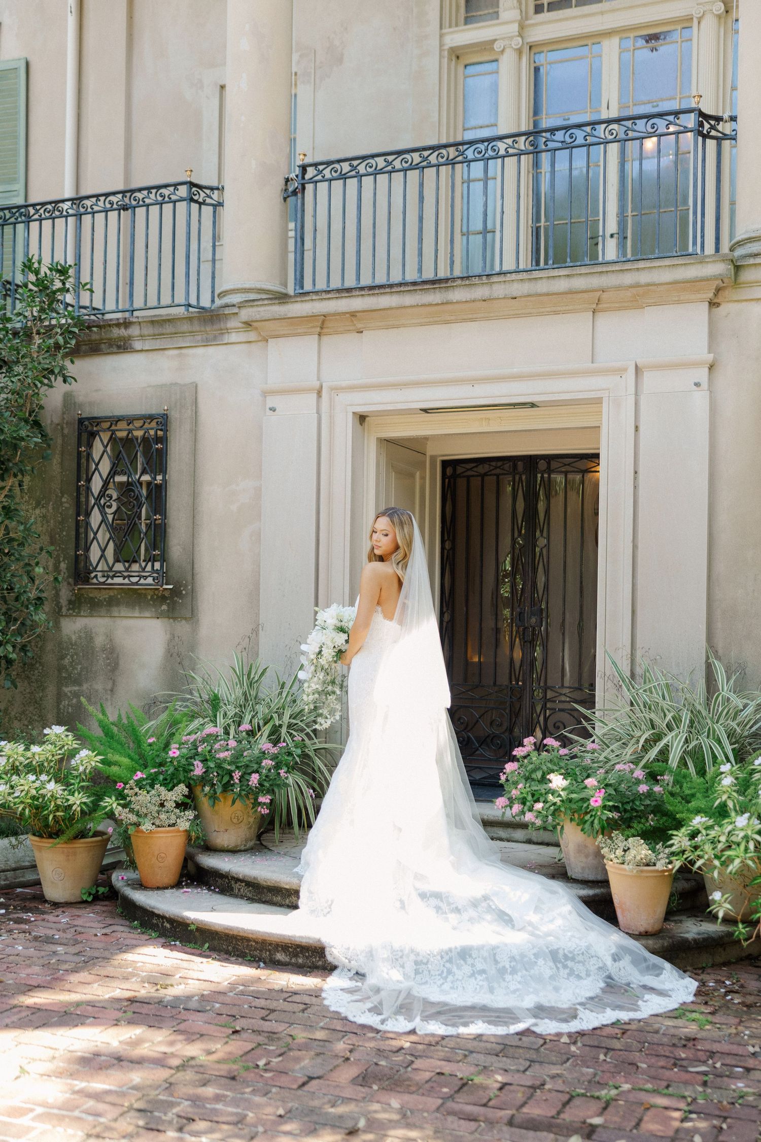 Stunning bridal gown with cathedral veil captured on brick steps of a historic mansion.