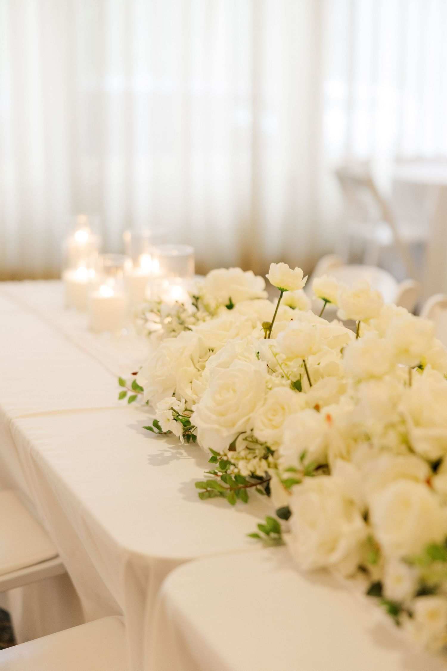 Elegant white rose centerpiece arrangement running along reception table.