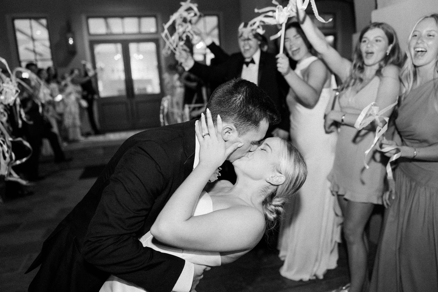 Wedding guests celebrate with joyful dancing in black and white photography.