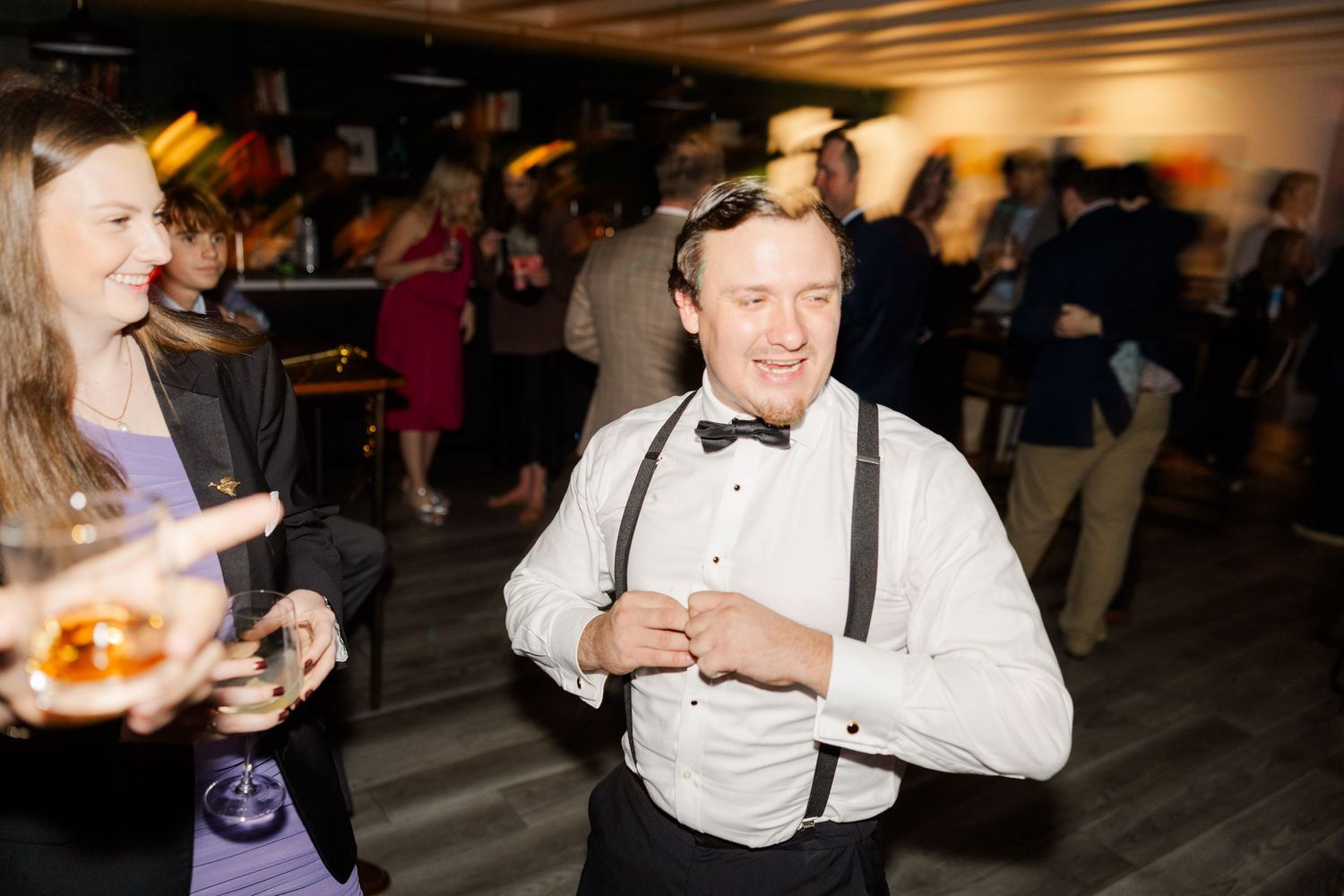 Wedding reception guests enjoying drinks and conversation in a dimly lit venue.