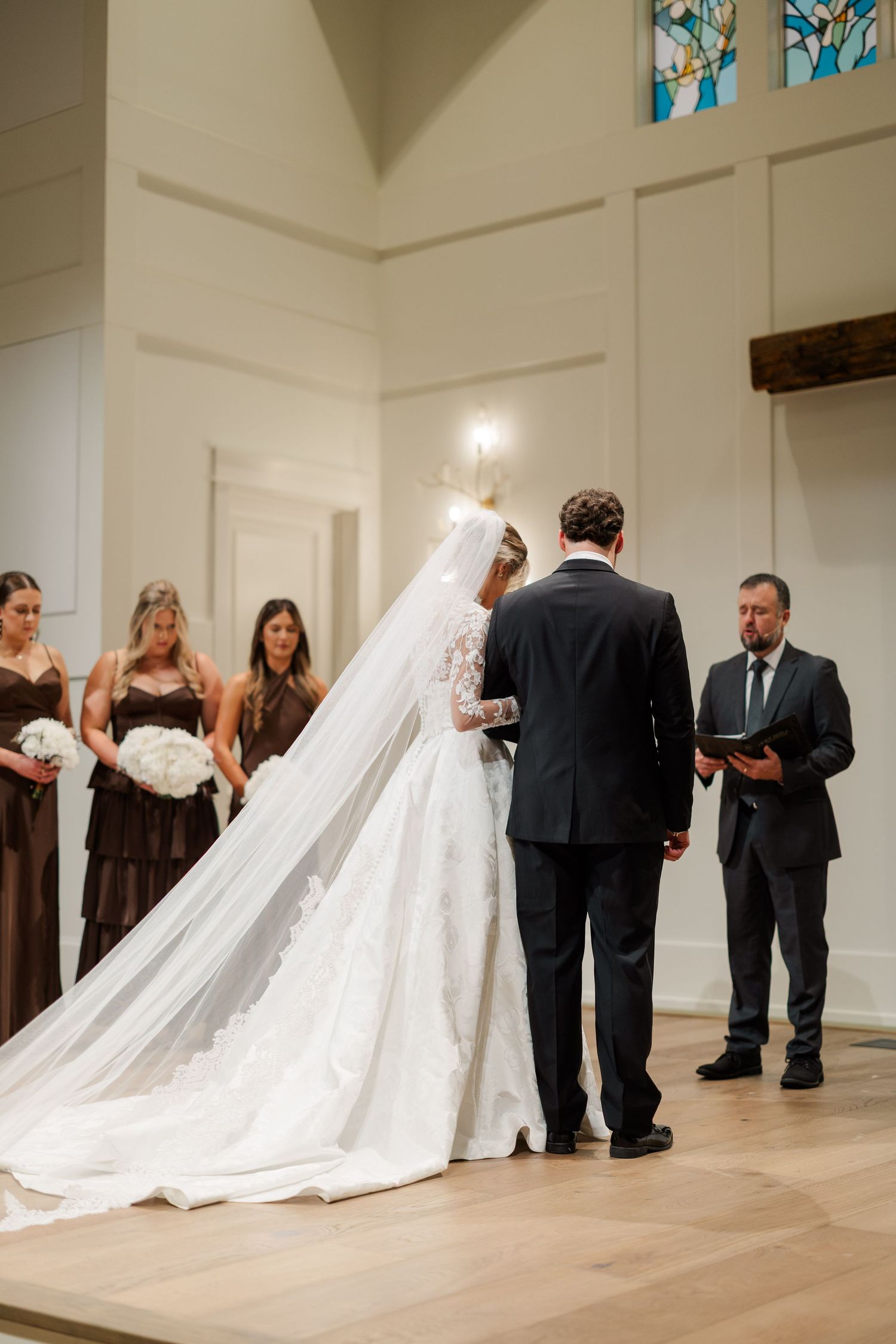 Wedding ceremony in a bright church with stained glass windows and flowing white dress.