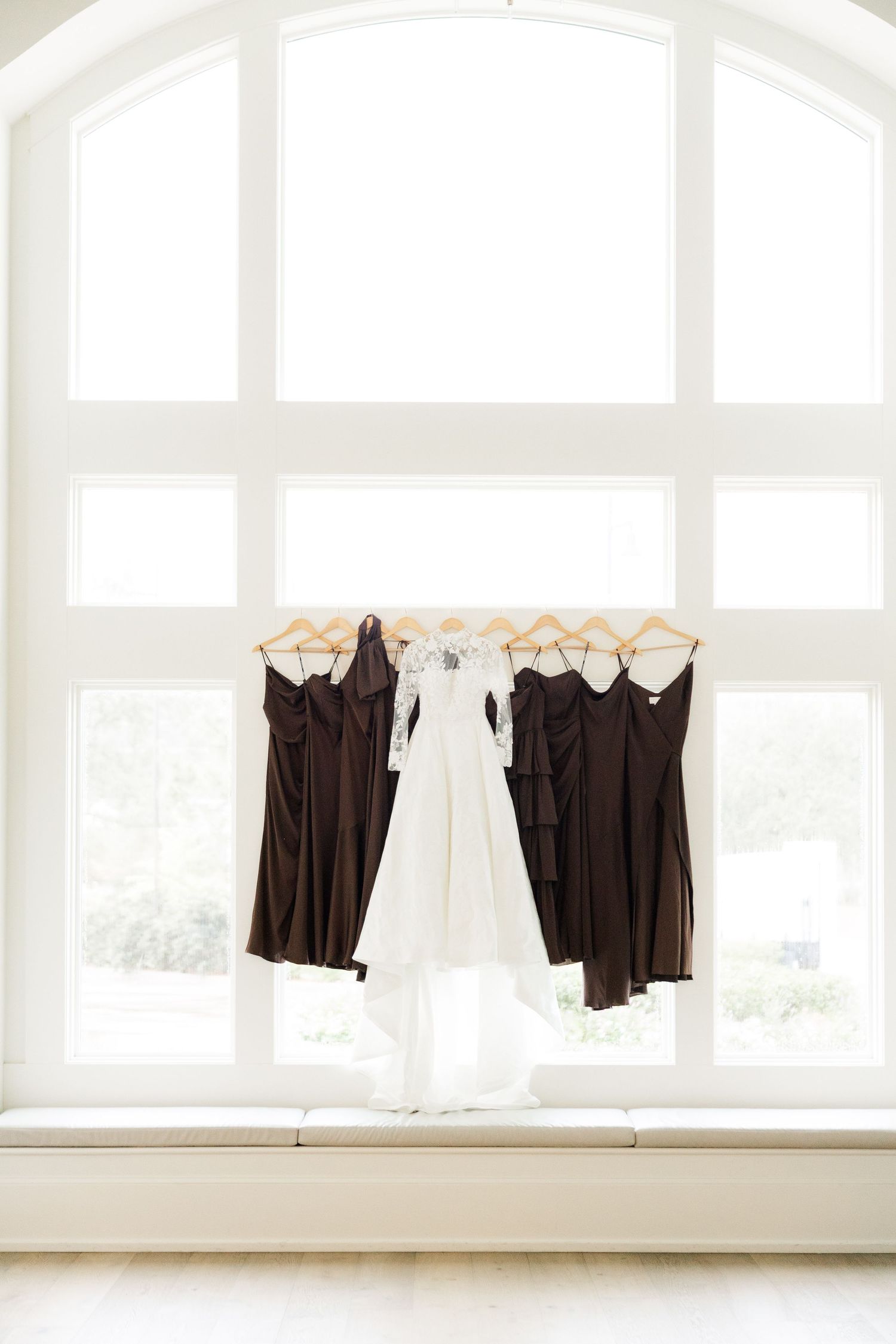 Wedding dresses and bridesmaids gowns hanging by a bright window in preparation for the big day.