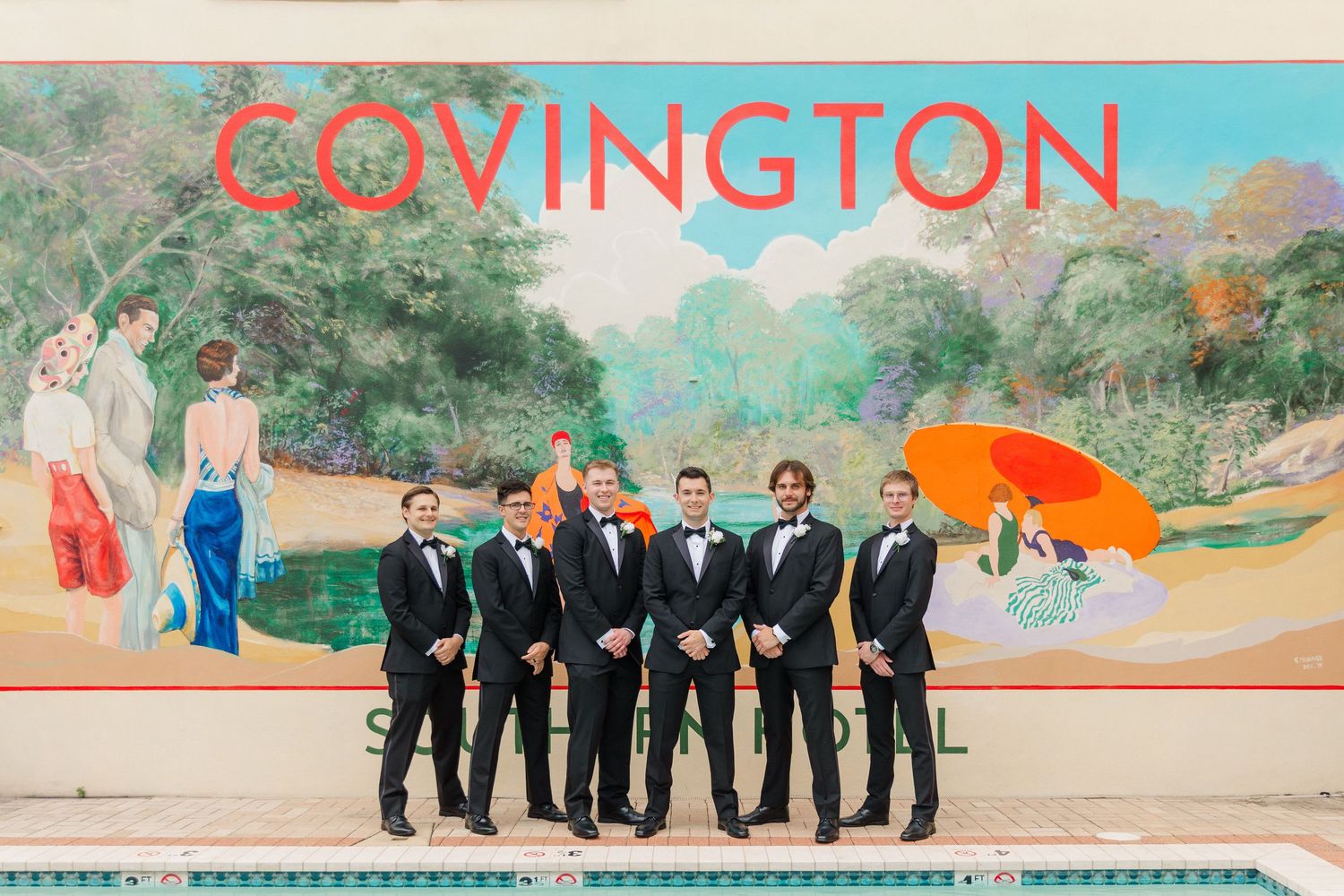 Wedding party in formal attire posed outdoors against a colorful Covington mural backdrop.