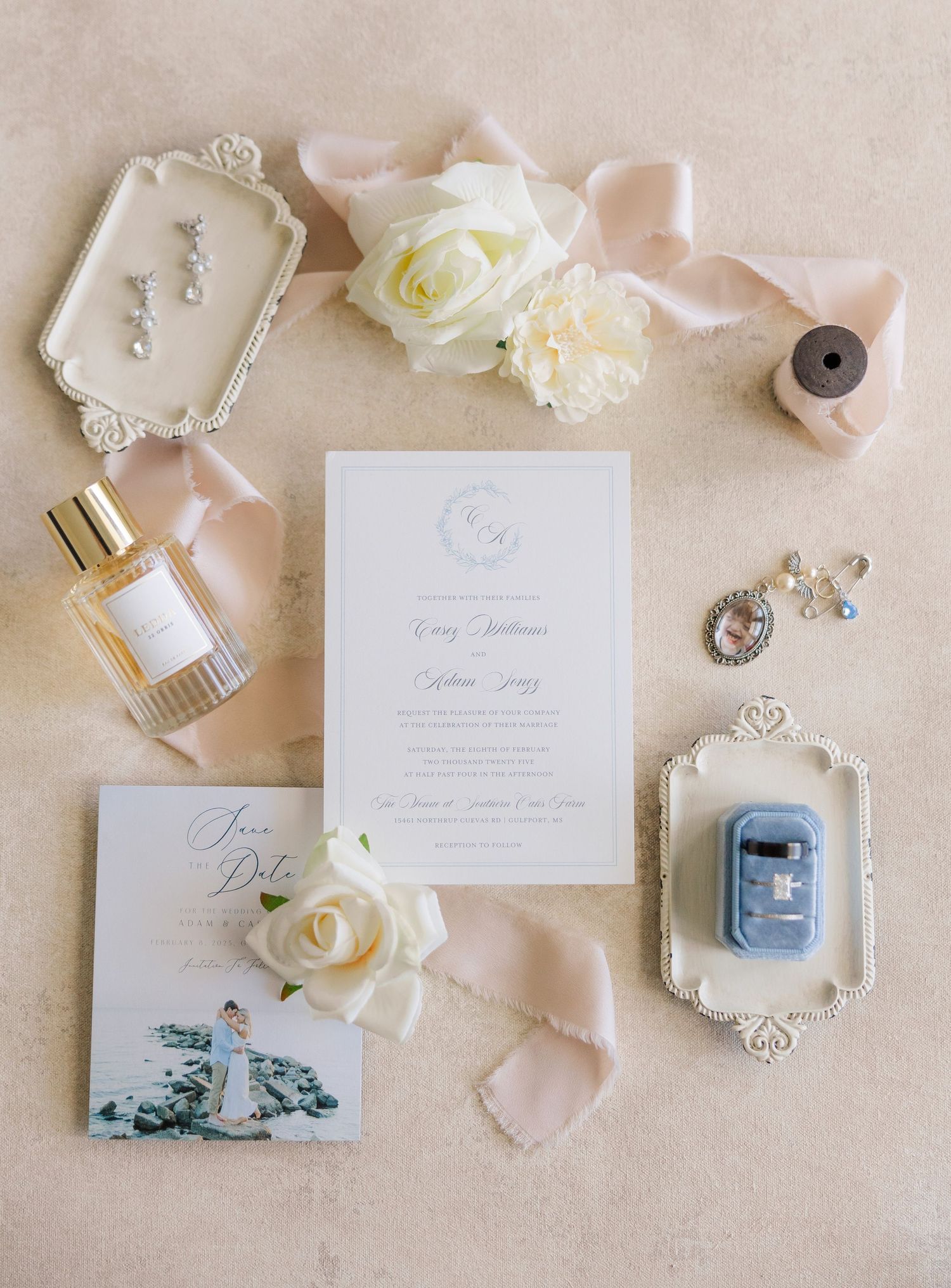 Wedding details flat lay with white invitation, roses, blush silk ribbon, perfume bottle and vintage jewelry on beige linen.